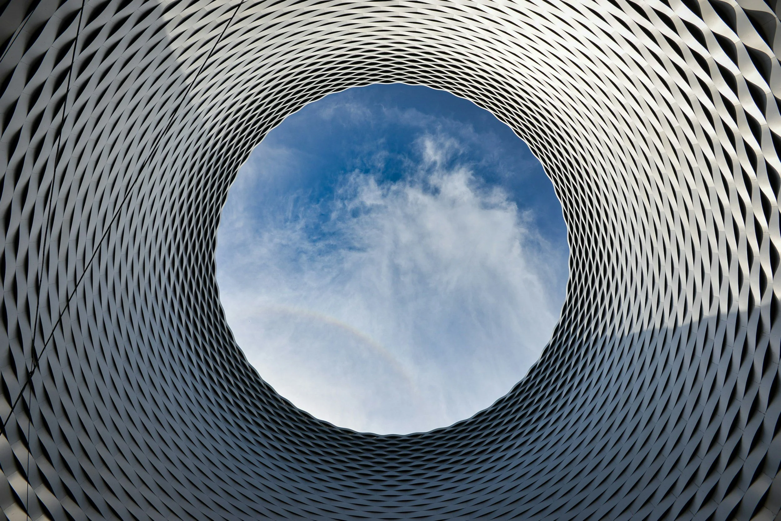 A circular architectural structure with a honeycomb pattern, looking upward at a blue sky with some clouds.