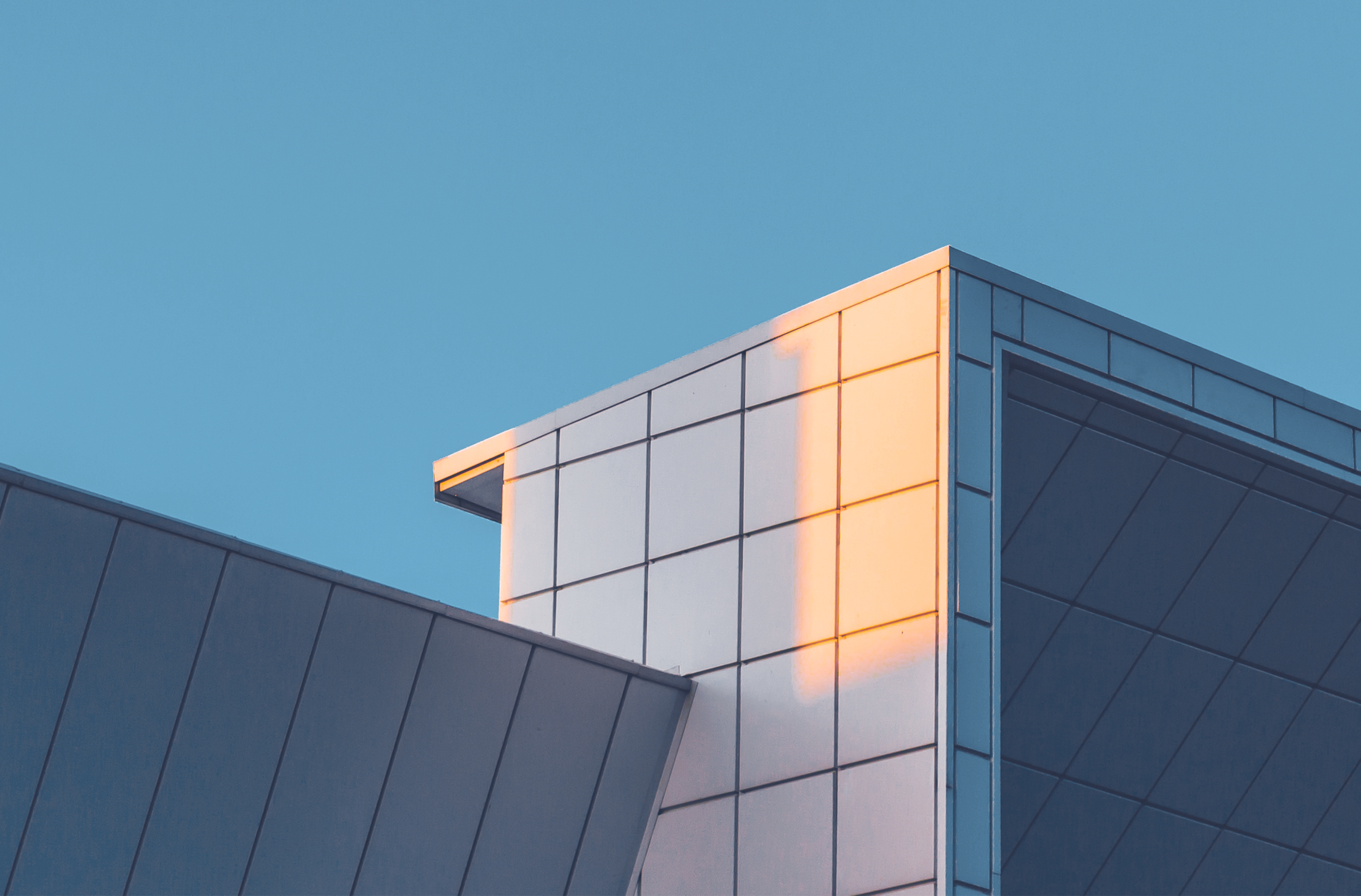 Close-up of a modern building with a sharp corner, reflecting sunlight, against a clear blue sky.