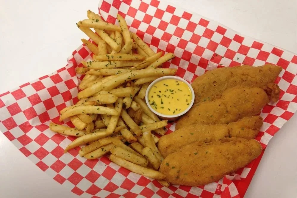 Fried fish fillets with seasoned French fries and a small cup of tartar sauce on red and white checkered paper.