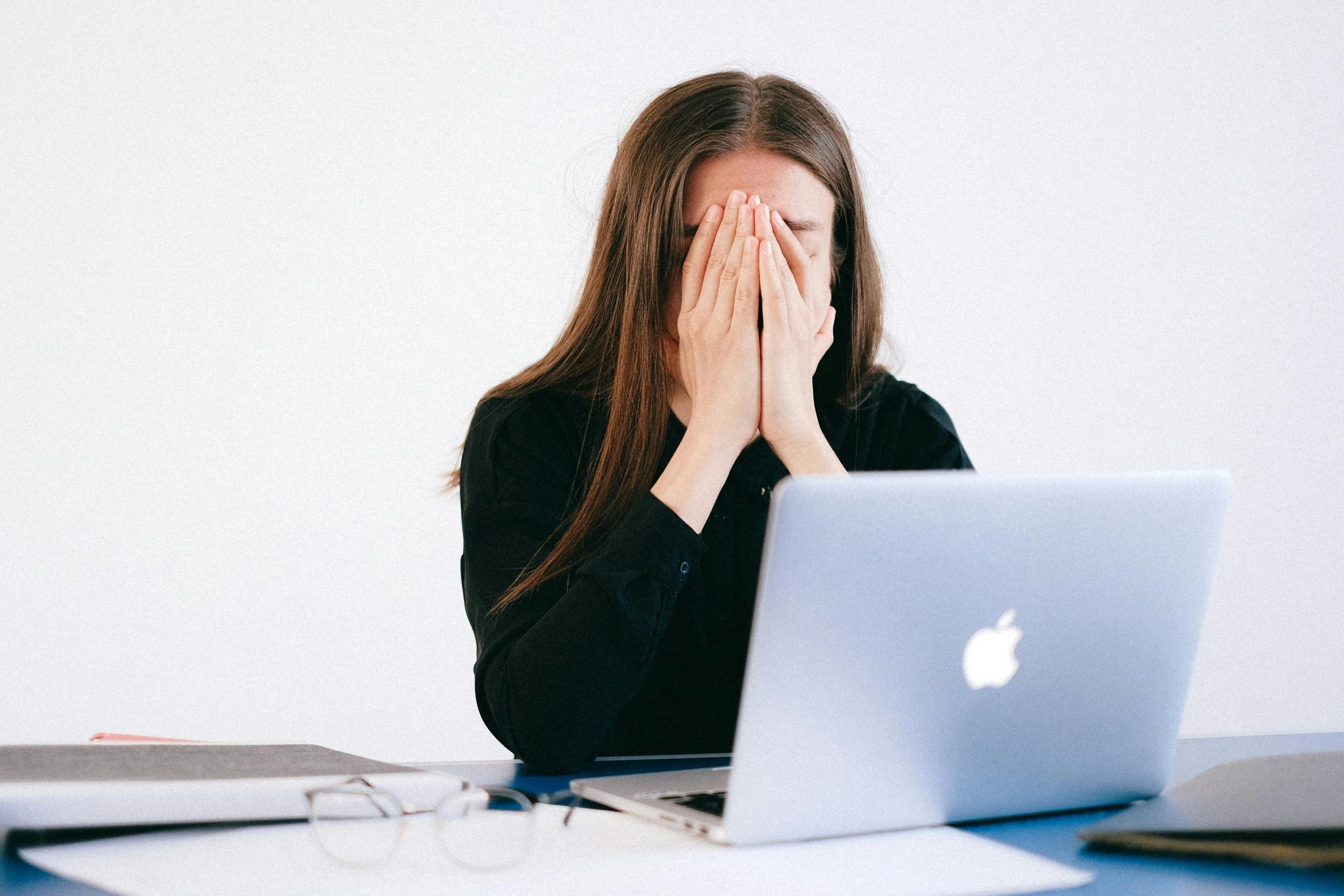 Woman feeling overwhelmed while working at her laptop, representing stress, competing priorities, and burnout.