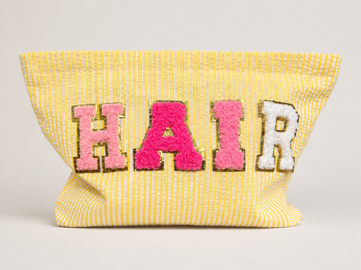 A yellow and white striped fabric bag with colorful, textured letters spelling 'HAIR' on the front.