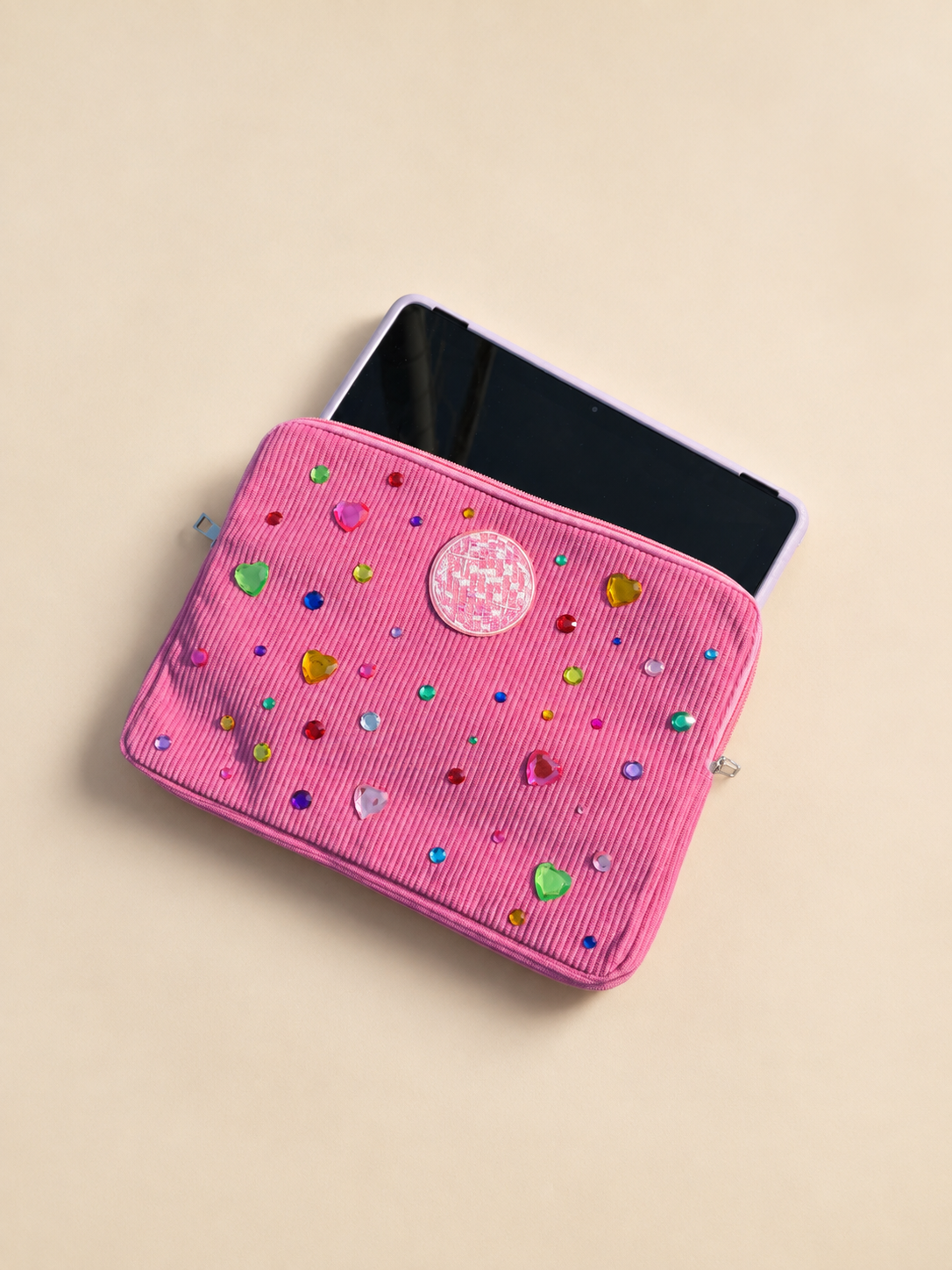 A pink zippered pouch decorated with colorful, multicolored and heart-shaped rhinestones, partially open with a smartphone inside, on a beige surface.