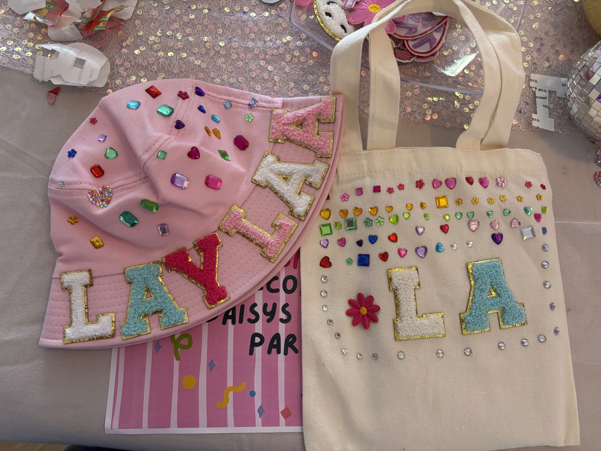 Colorful, decorated drawstring bags with rhinestones, patches, and lettering on a patterned background.