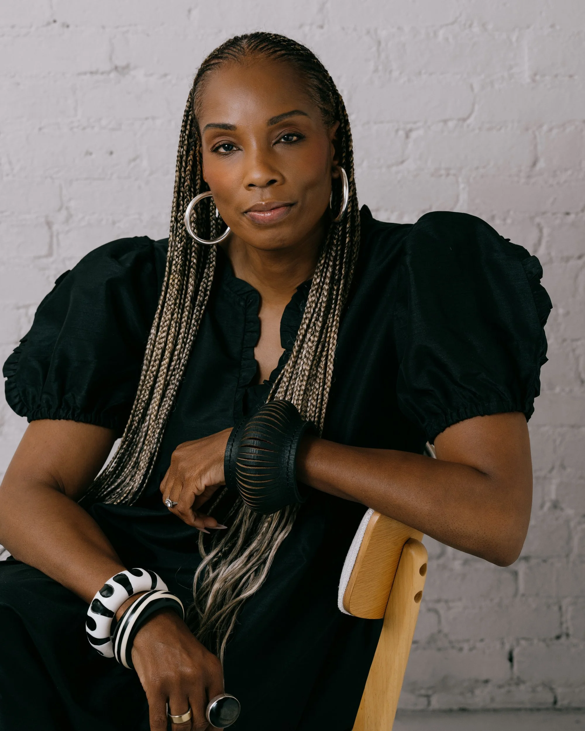 Sherise Bright seated with her arm over the back of a wooden chair, looking directly at the camera.