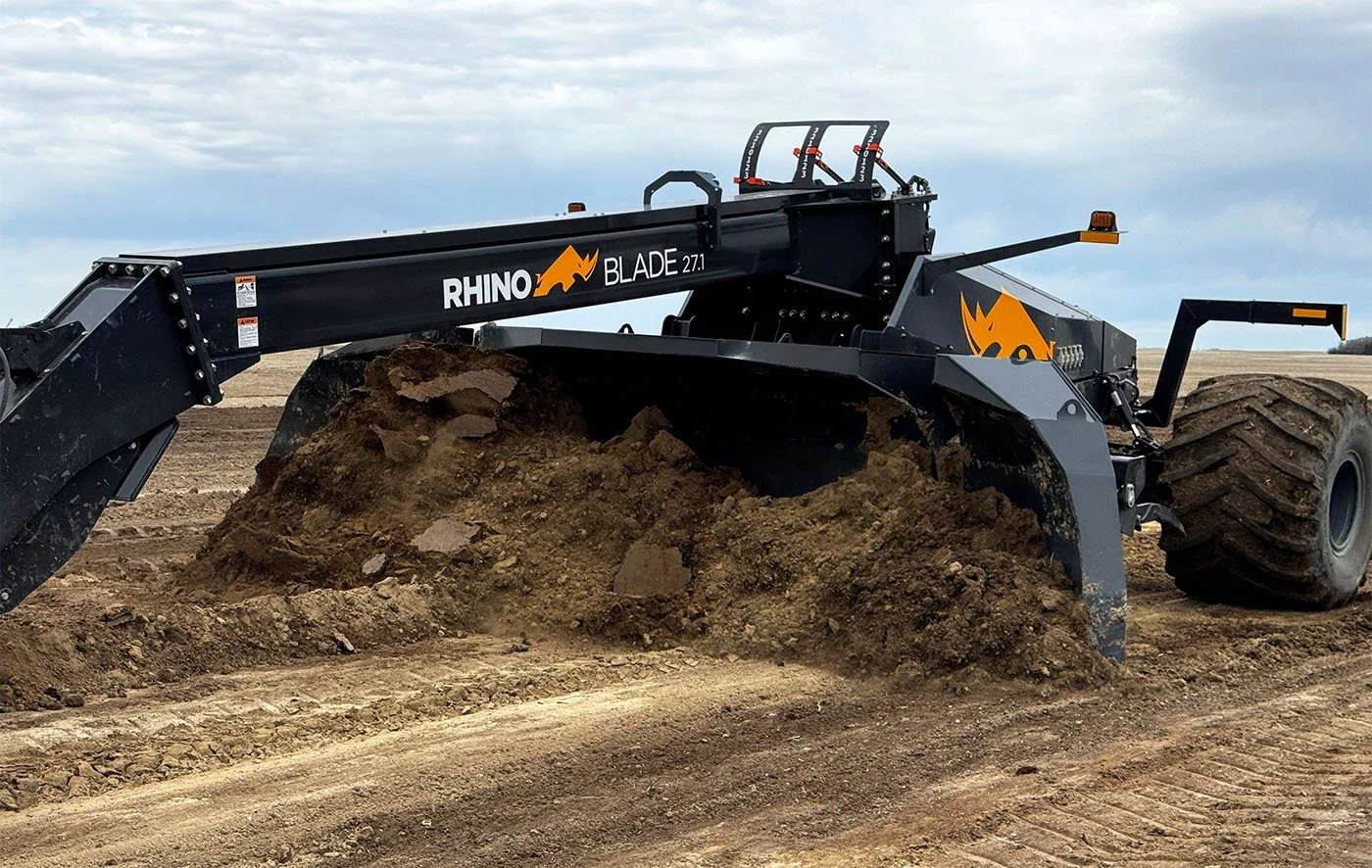 A large black Rhino Blade 27.1 bulldozer clearing dirt on a construction site with open land and cloudy sky in the background.