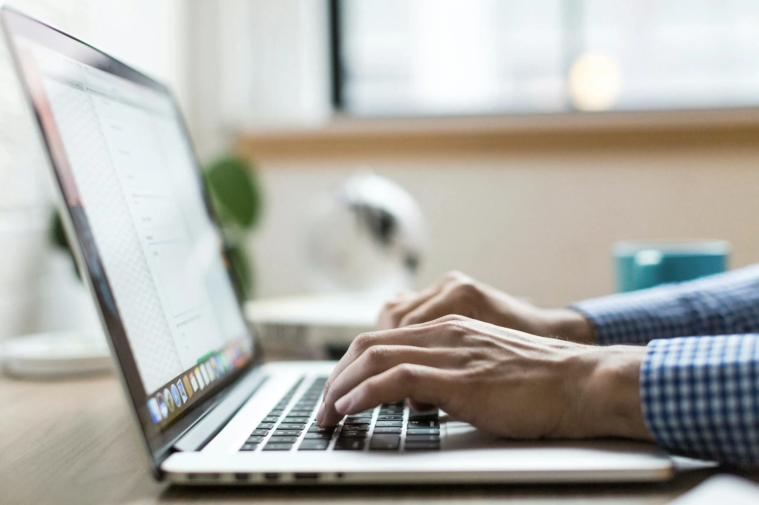 Close-up of a person's hands typing on a laptop computer keyboard in an indoor setting with natural light.