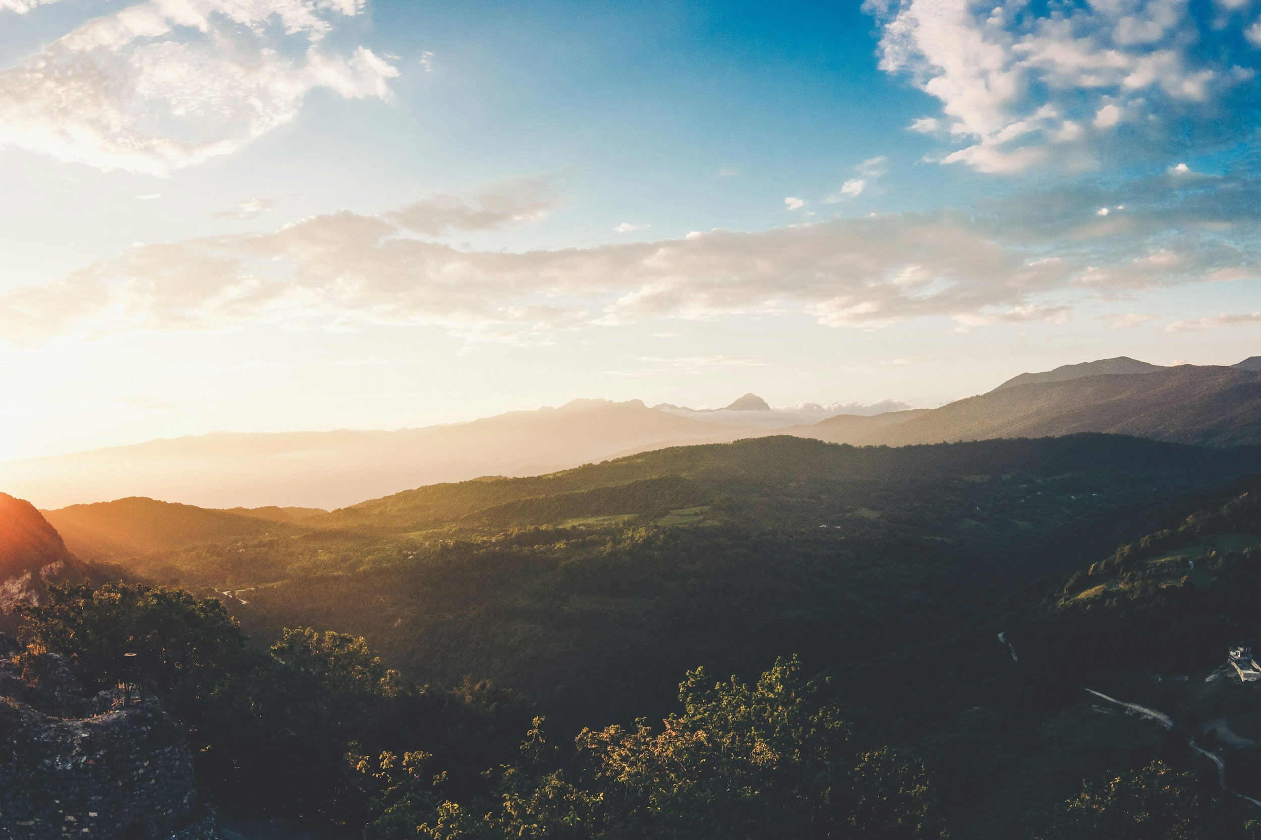 Scenic view of mountains with a partly cloudy sky at sunset, casting a warm glow over the landscape.