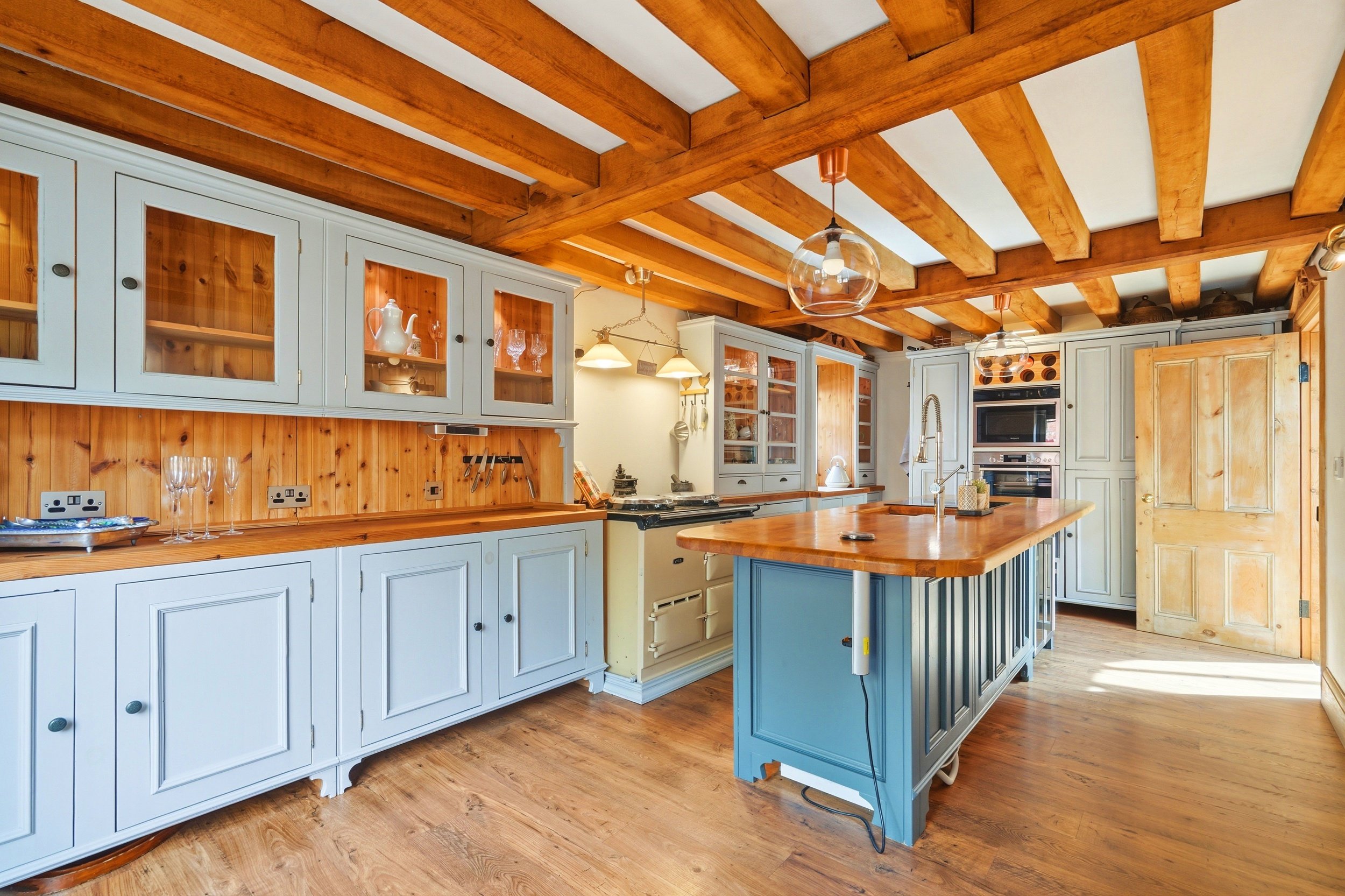 Kitchen with wooden ceiling beams, white and light blue cabinets, a kitchen island, and hardwood floors.