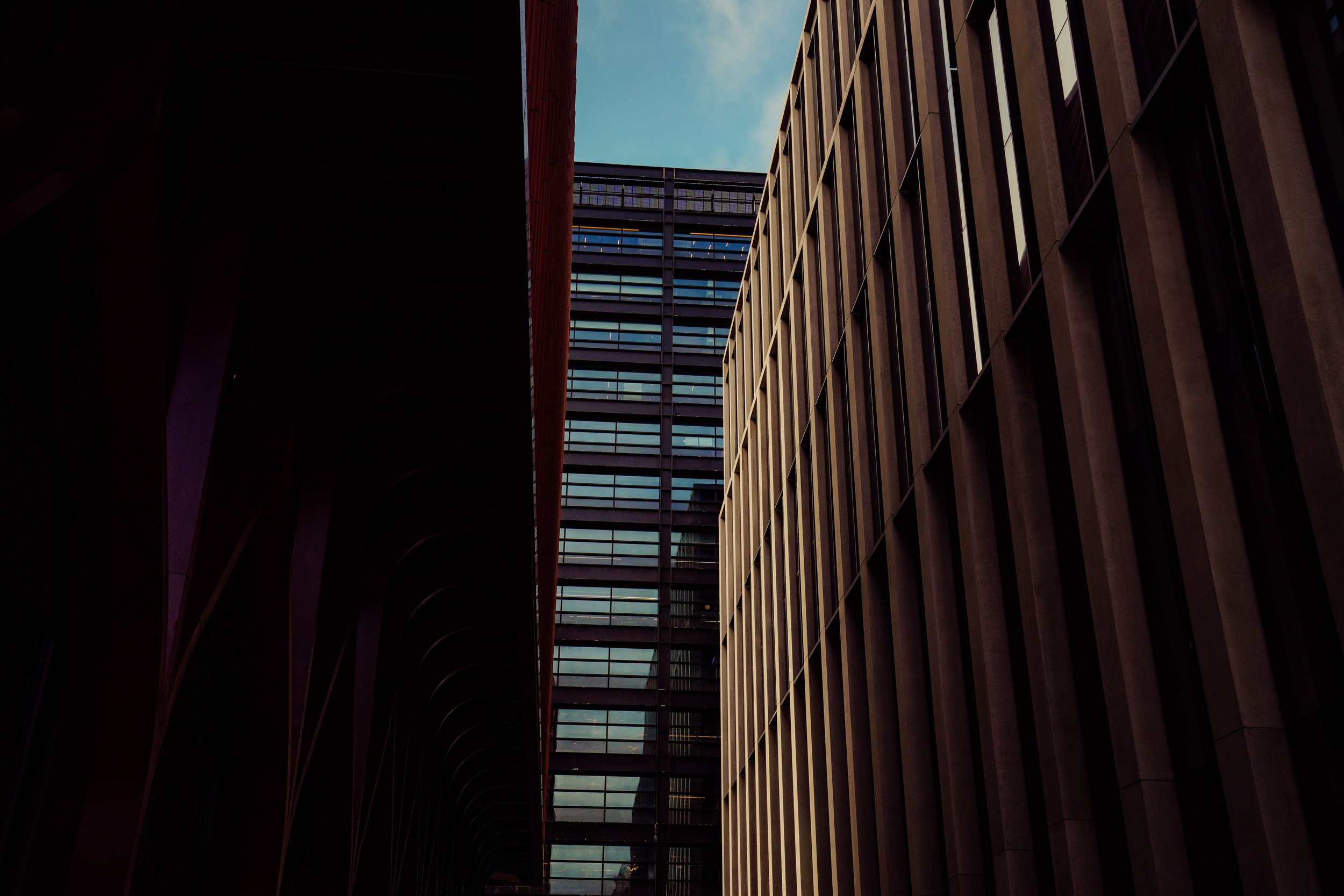 Looking up at tall modern buildings with glass windows, with a partly cloudy sky in the background.