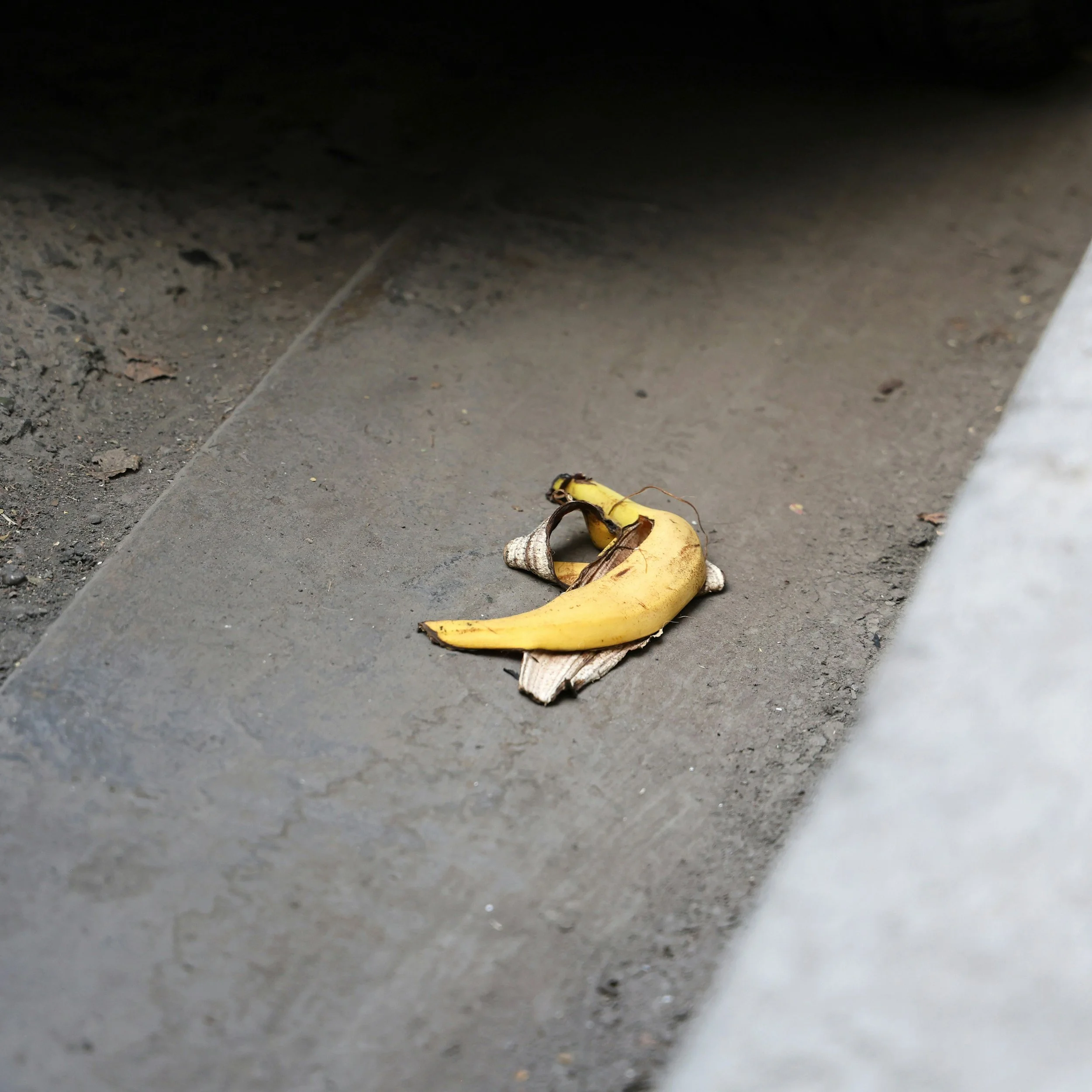 Close-up of a discarded banana peel on a sidewalk near a curb.