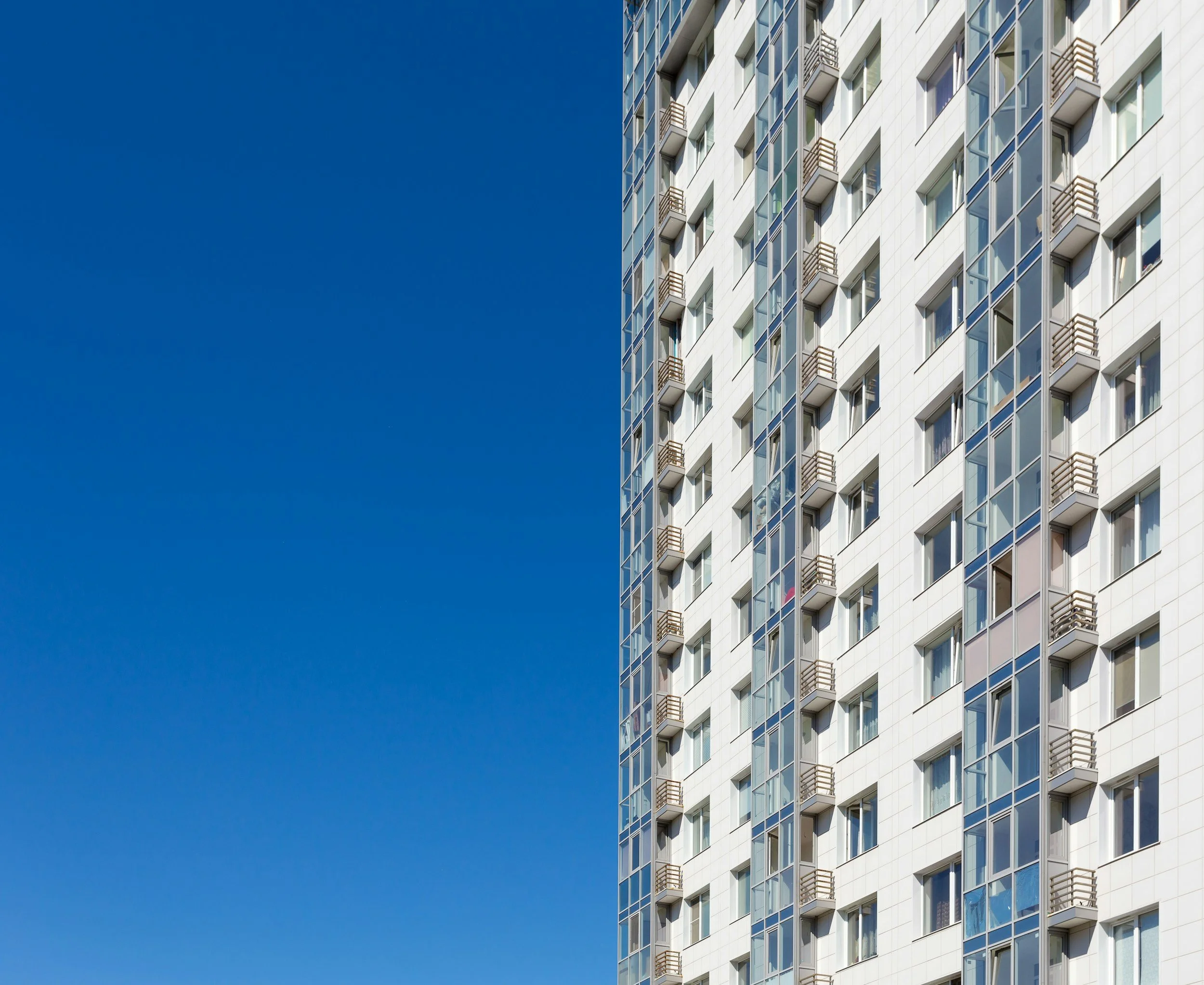 Close-up view of a modern high-rise apartment building with multiple balconies and large windows, against a clear blue sky.