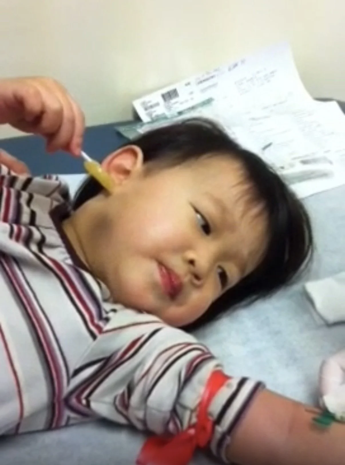 Child lying in a hospital bed receiving a bloodwork in their arm from a healthcare worker.