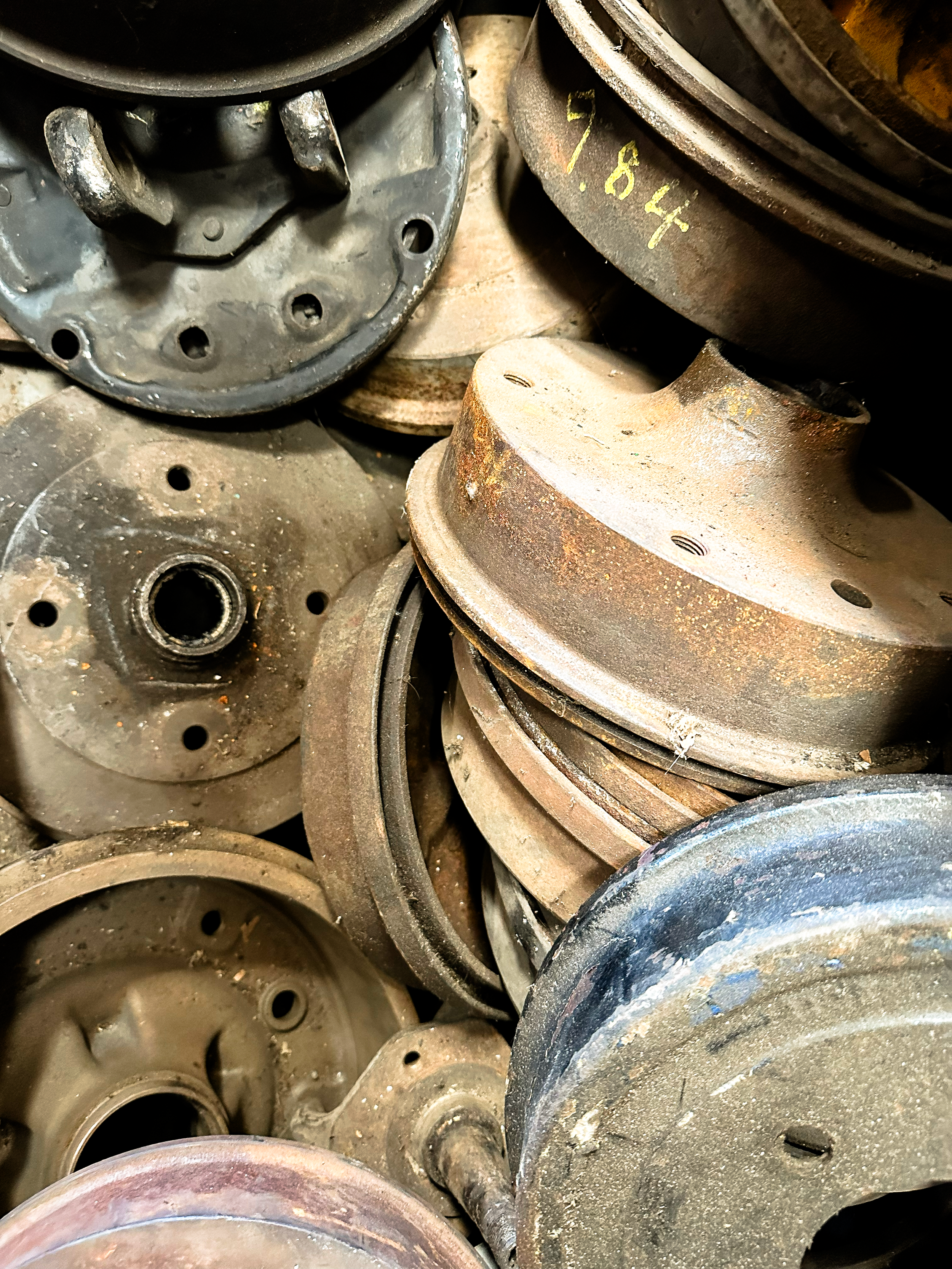 A stack of used and rusty metal train wheels or trolleys, some with holes and rust, piled together.