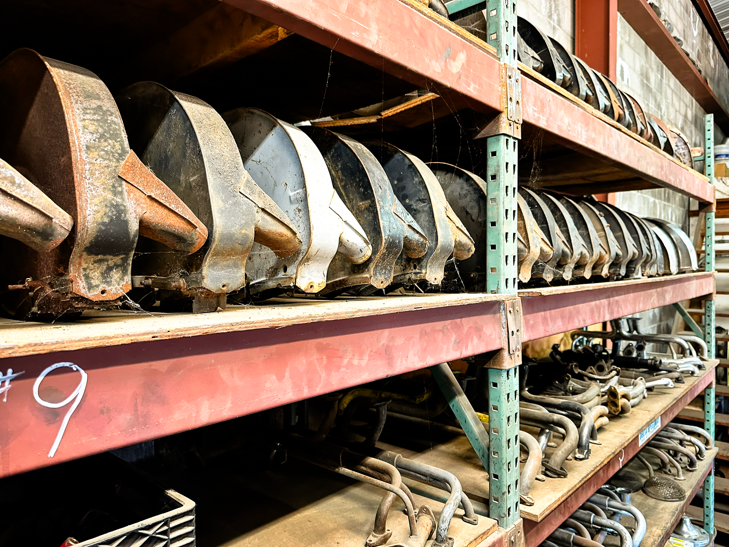 Shelf filled with old, rusty metal car exhaust pipes stored in a warehouse.