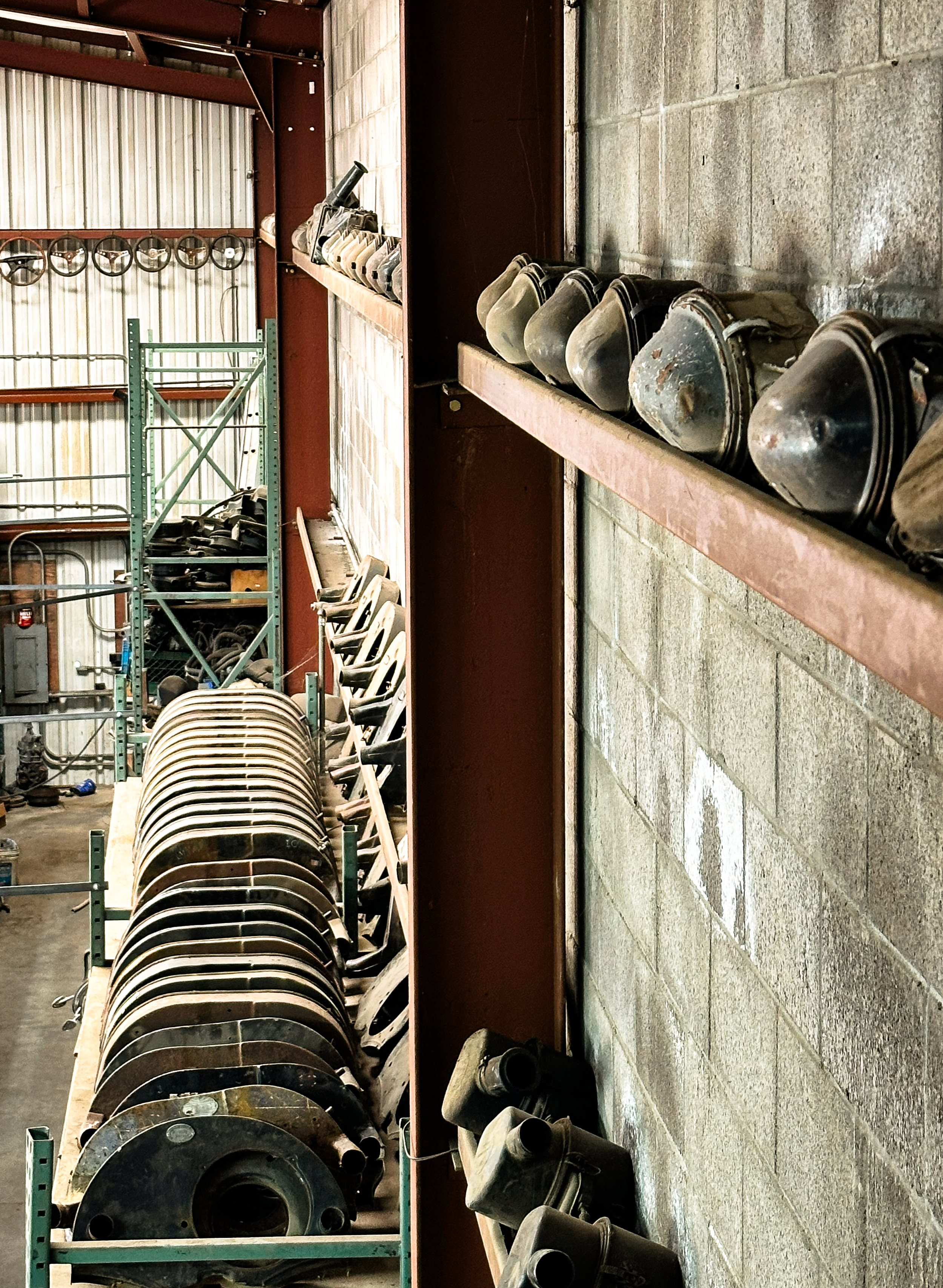 Industrial storage of various large metal parts and equipment on metal shelving in a warehouse.