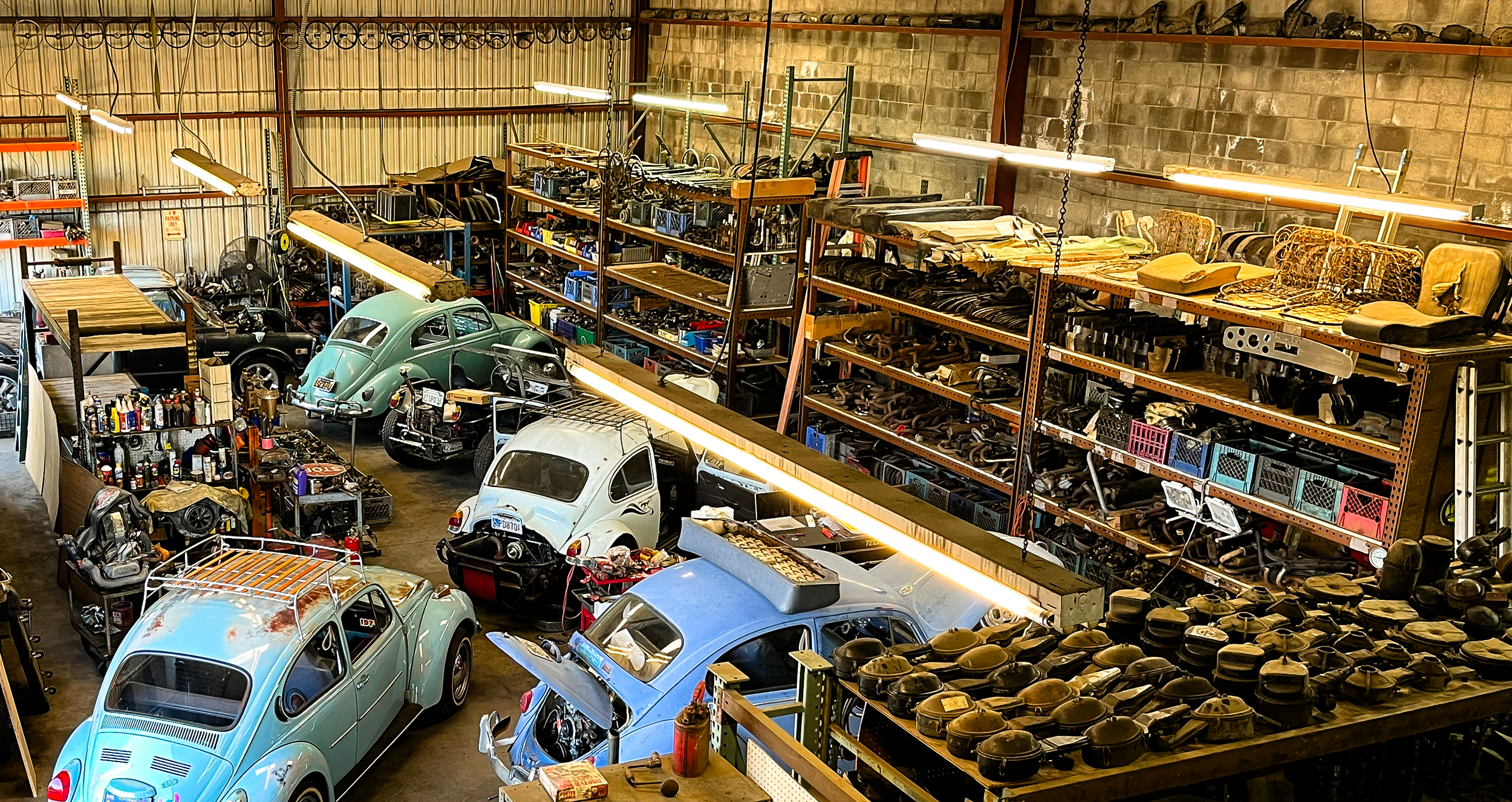 Interior of a garage or warehouse filled with vintage cars, shelves holding car parts, and various tools.
