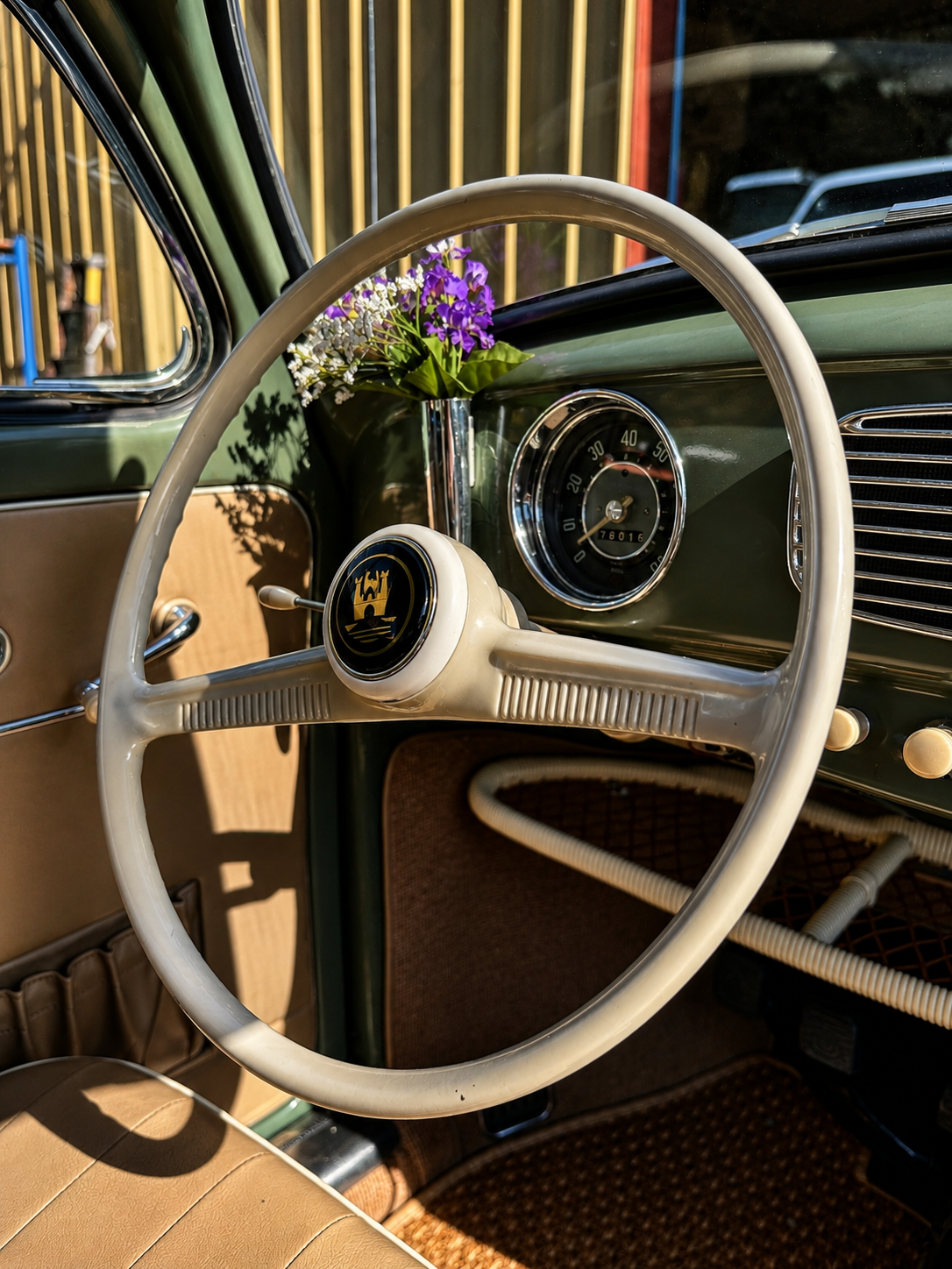 Classic Volkswagen Beetle interior featuring an ivory steering wheel, original dashboard, and fresh flowers in the iconic dash-mounted vase.