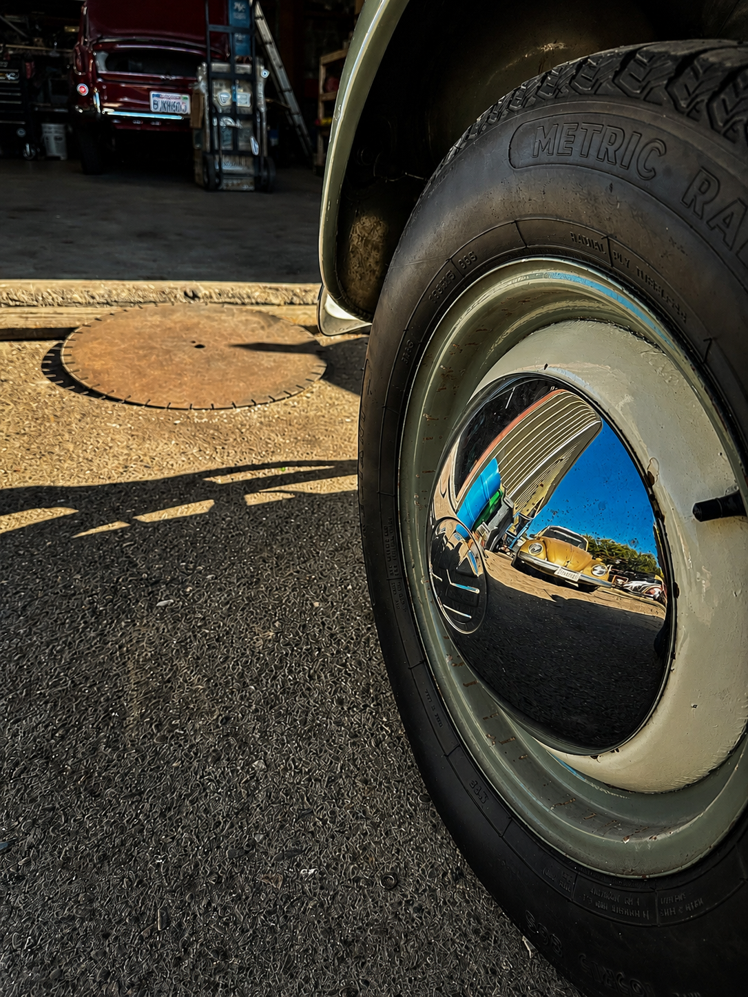 Chrome Volkswagen hubcap reflecting a classic gold Beetle outside the BenBuilt Customs restoration shop.