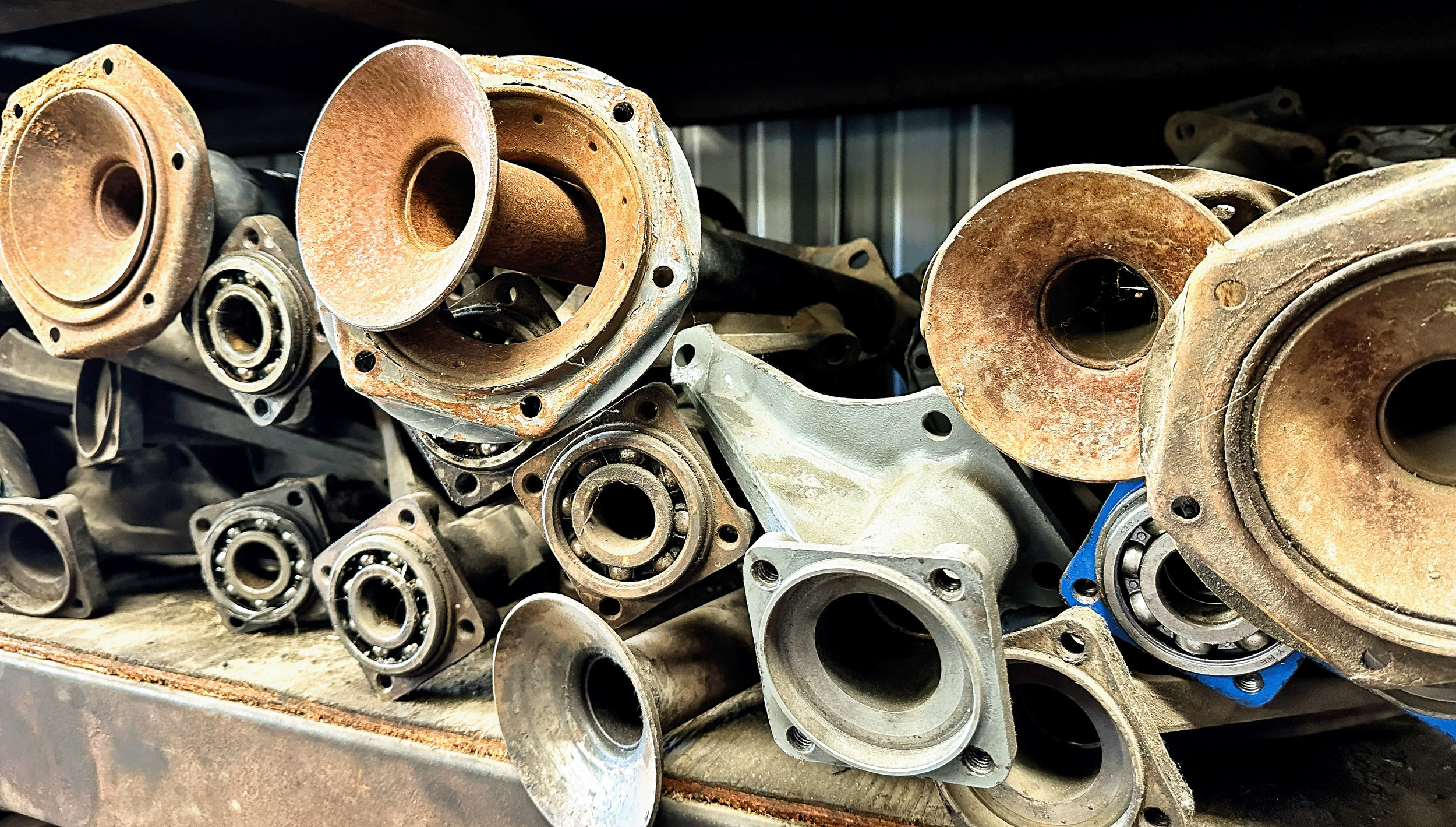 A collection of rusty and metallic engine parts, including cylinder heads and bearing components, stacked on a workbench in a workshop.