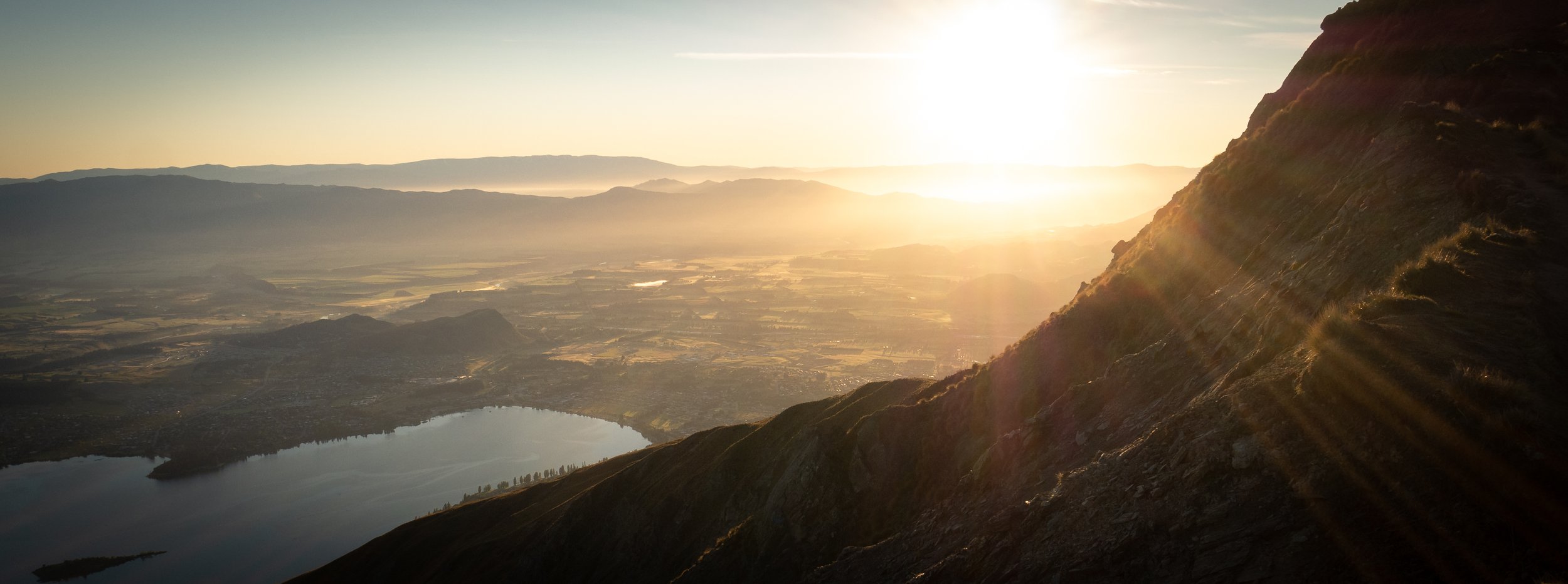 Sunrise over a Mt Roy, with a lake and valley below, and sunlight casting rays over the landscape - Wanaka, New Zealand