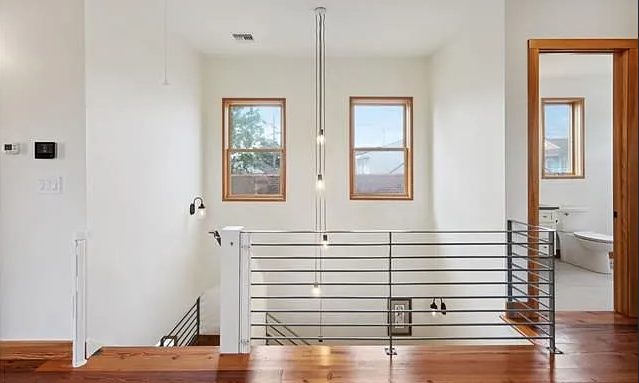 A modern minimalist interior with two windows, a staircase with metal railing, and a door leading to a bathroom.