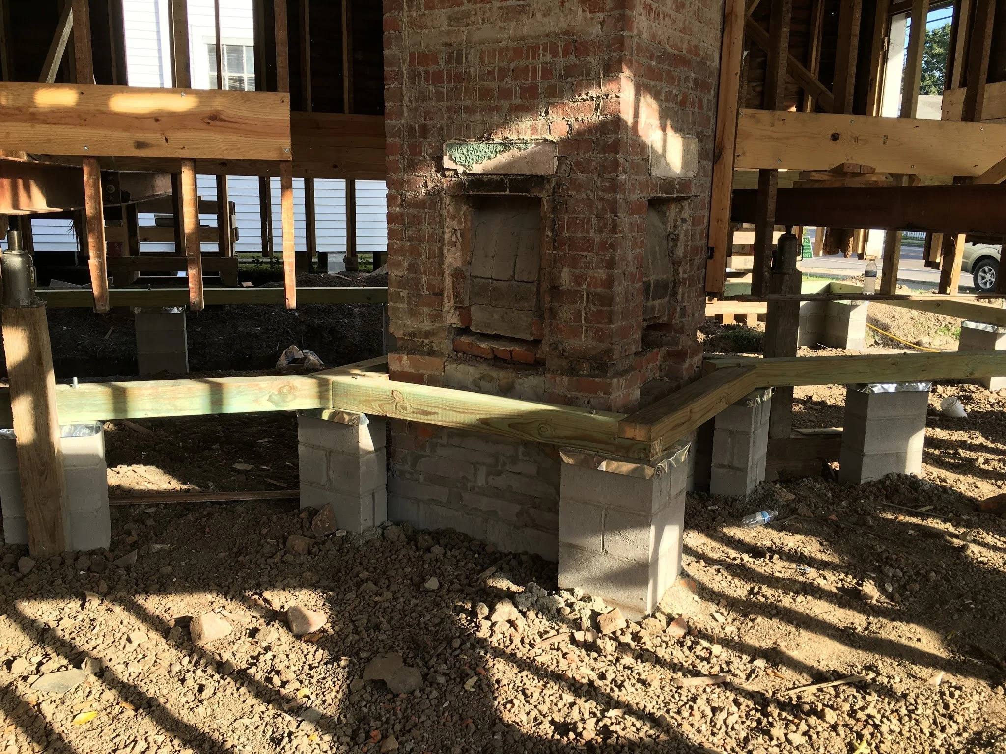 Construction site with a brick chimney and wooden framing for a house. Soil and debris on the ground, with a water bottle visible in the background.