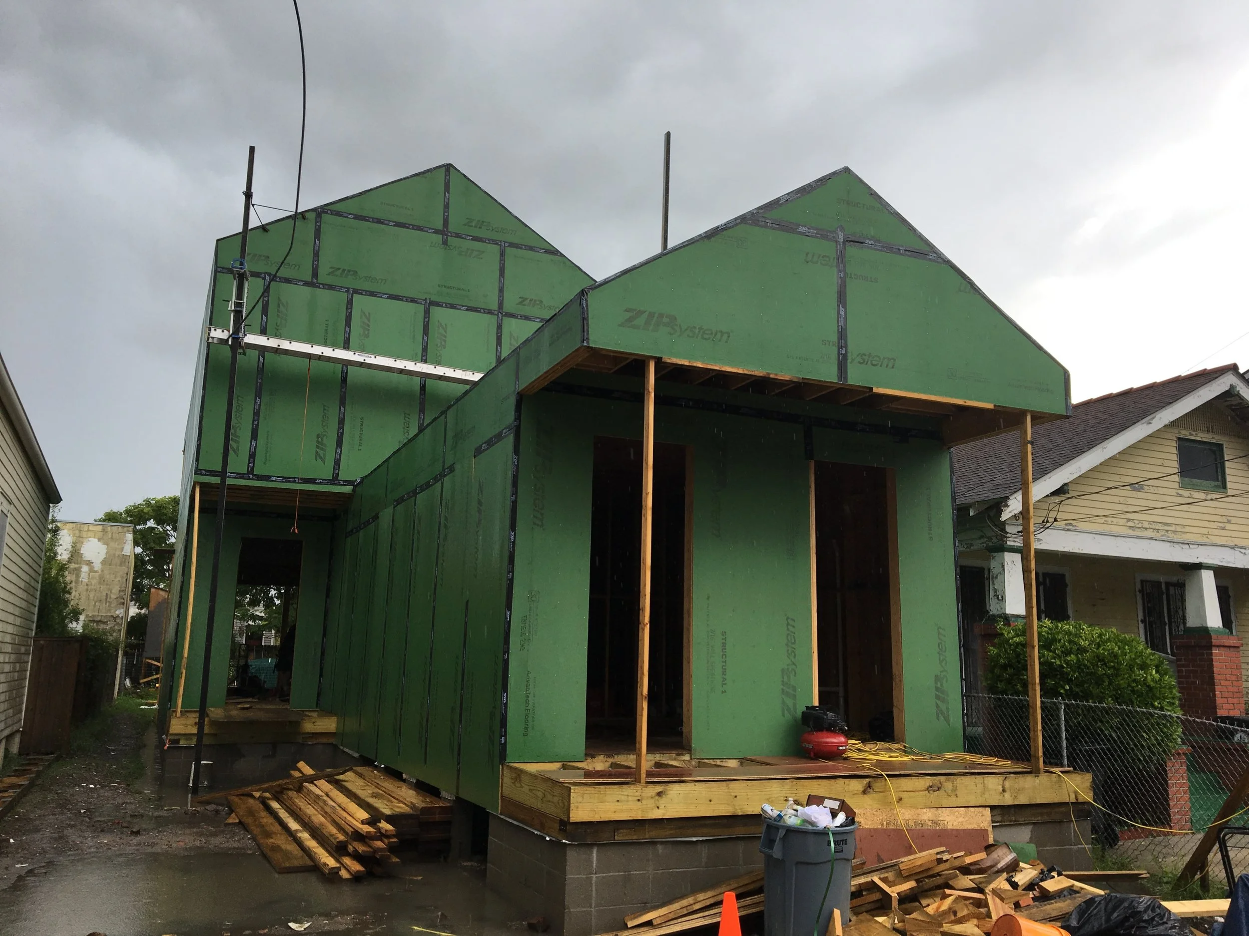 Construction site of a house with green sheathing boards and wooden framing, rain clouds overhead.