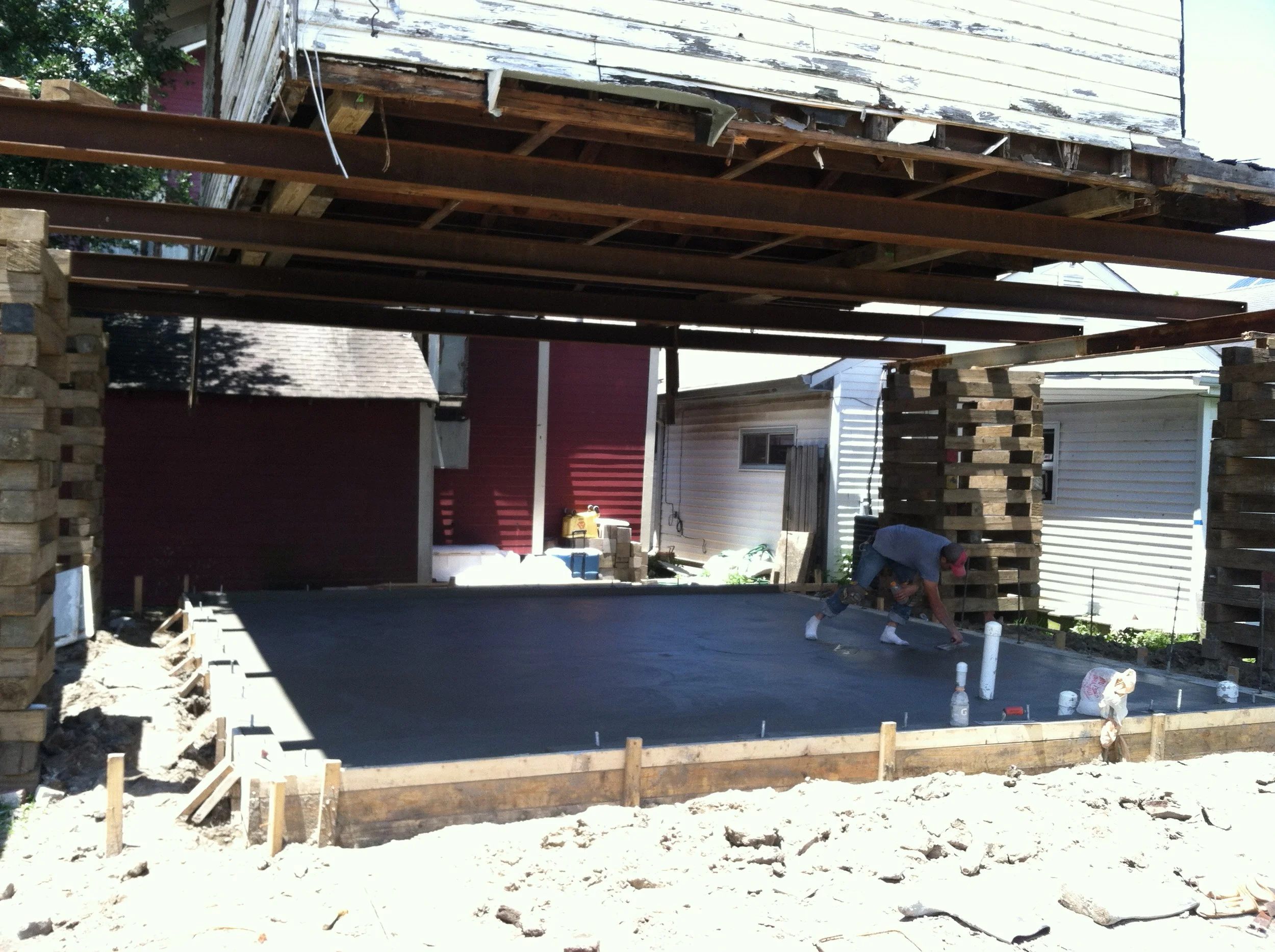 Construction site with a raised wooden deck supported by brick pillars, workers, and building materials.
