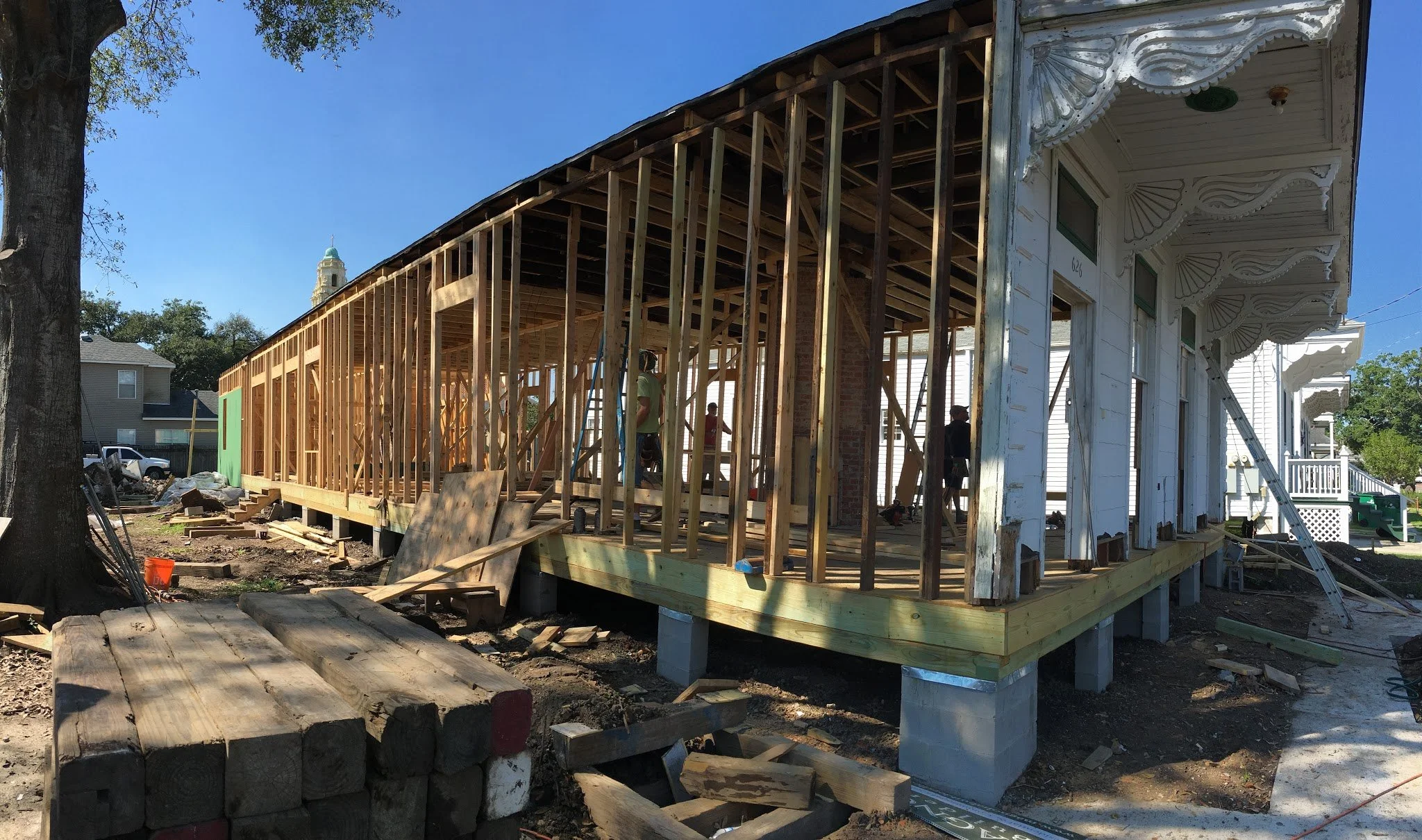 Construction of a new porch or extension on a house with workers assembling wooden framing under a clear sky.