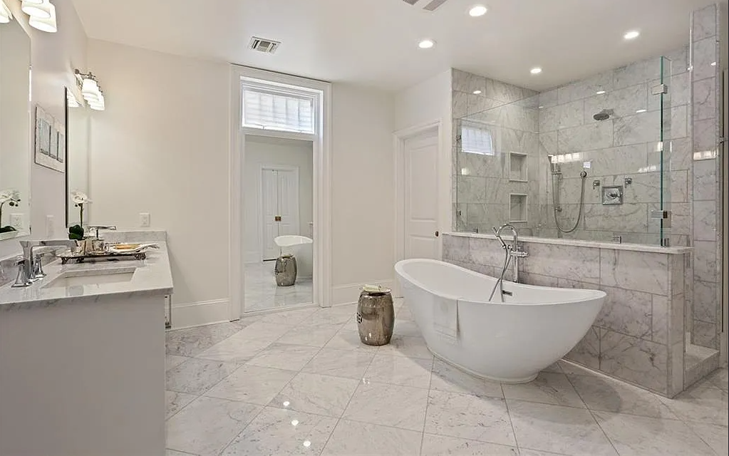 A luxurious bathroom with a white freestanding bathtub, marble tiled walls and floors, a walk-in shower with glass enclosure, white cabinets, and a double sink vanity.