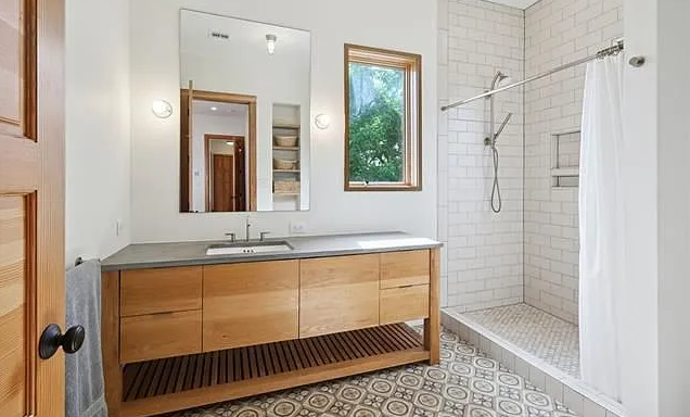 Bathroom with a wooden vanity, large mirror, window with trees outside, and a walk-in shower with white tiles and a shower curtain.