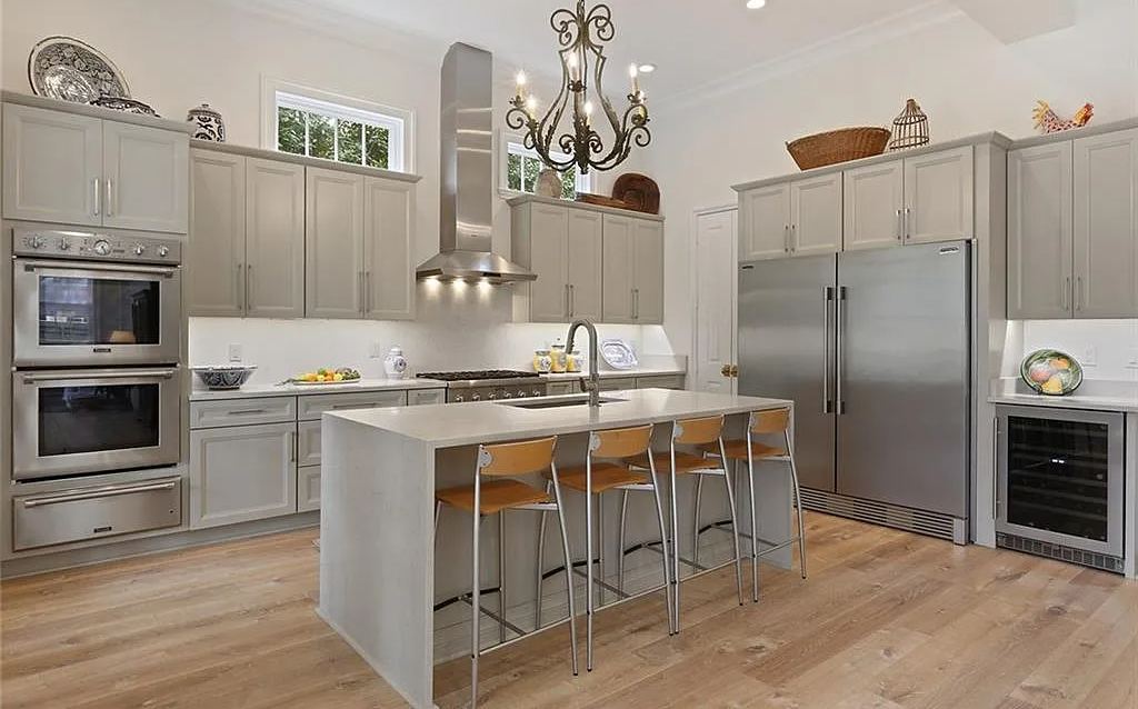 Modern kitchen with gray cabinets, stainless steel appliances, a central island with three chairs, hardwood floors, and decorative items on top of the cabinets.