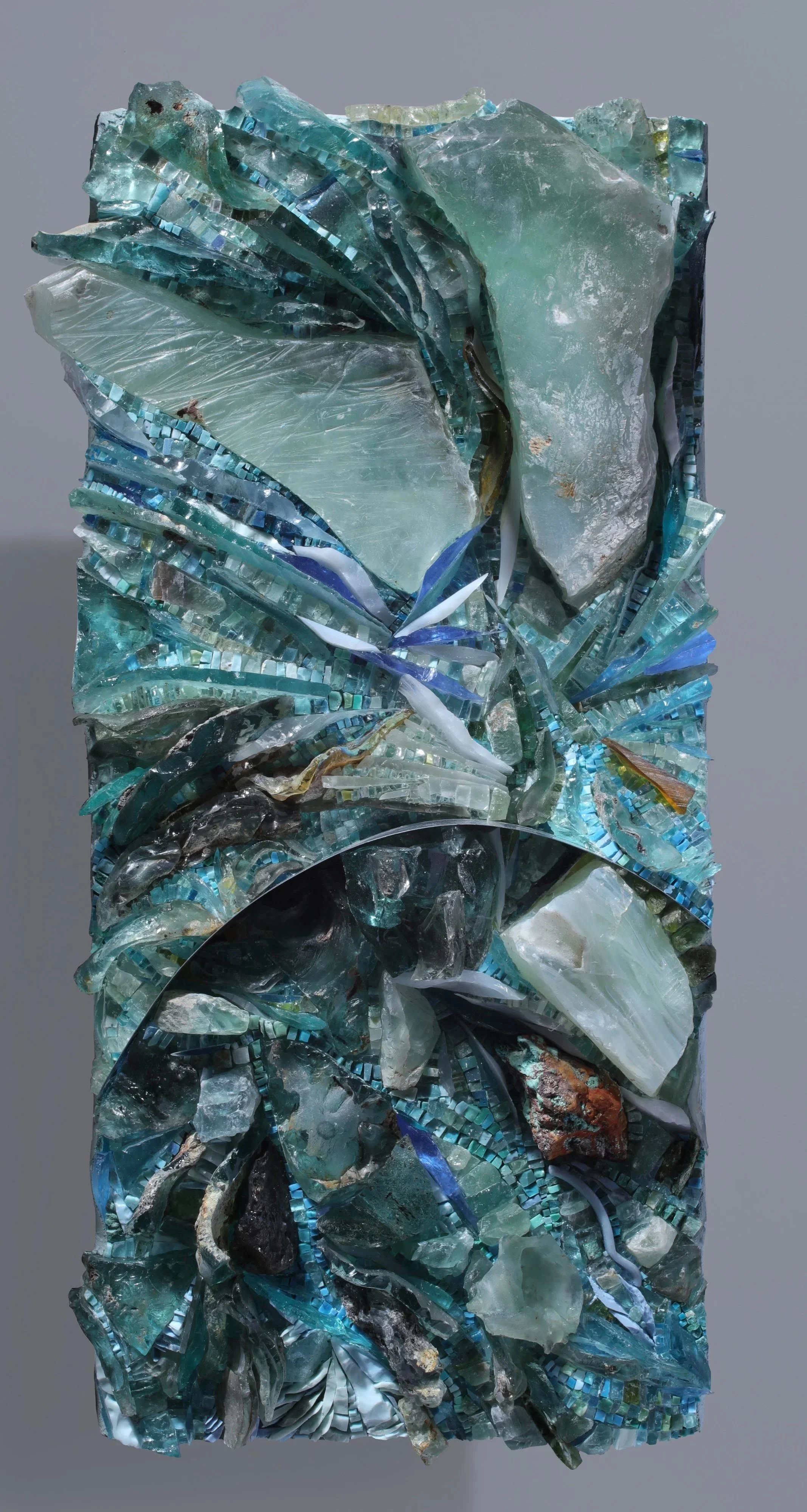 Abstract sculpture made of various pieces of colored glass, tile, and aquamarine stones, arranged in a chaotic and textured pattern.