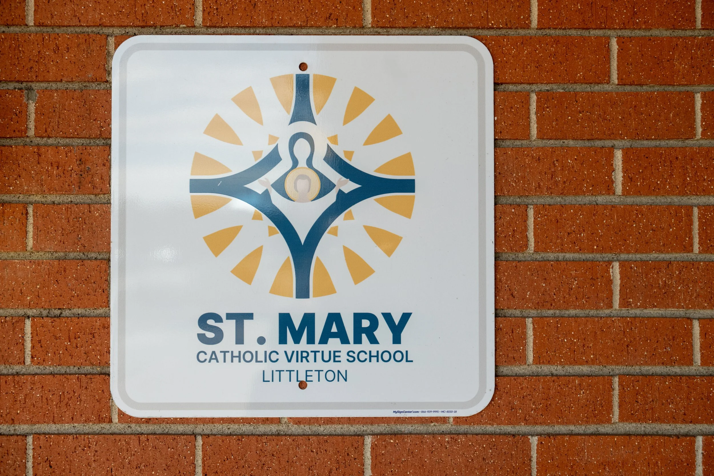 A school sign that reads 'St. Mary Catholic Virtue School Littleton' on a brick wall.
