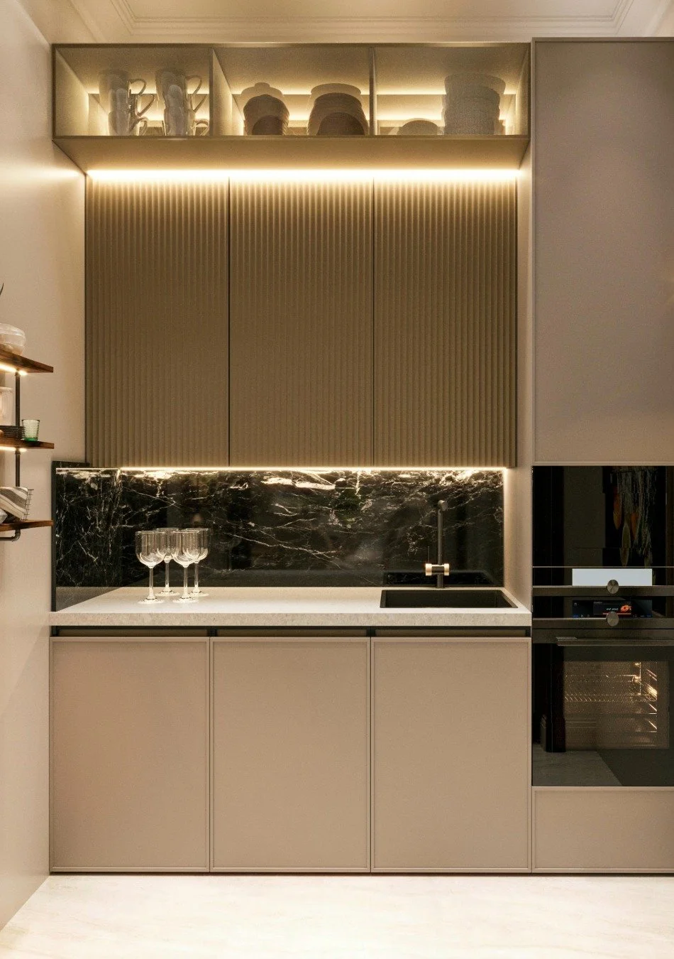 Modern kitchen with beige and black marble accents, upper glass cabinets with dishes, black sink, built-in oven, wine glasses on counter.