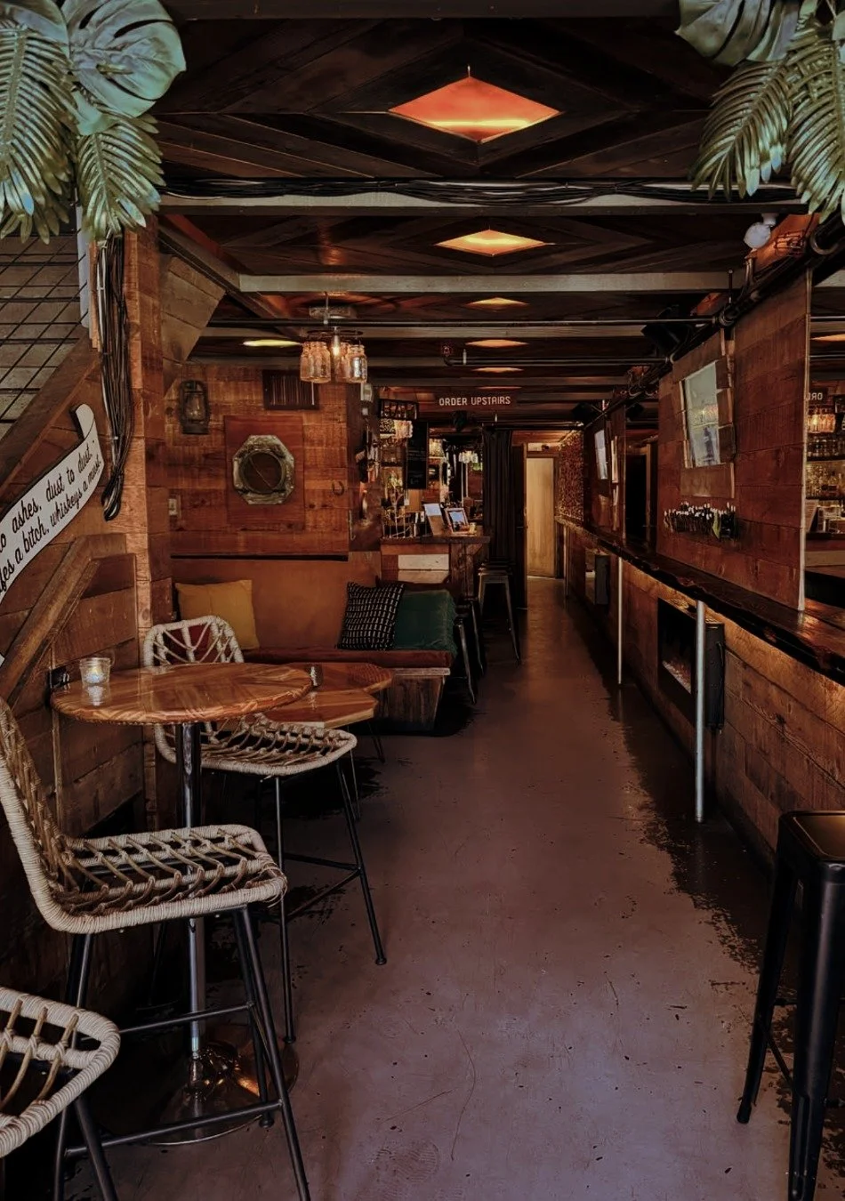Interior of a cozy bar with wooden decor, high-top tables, woven chairs, and warm lighting.
