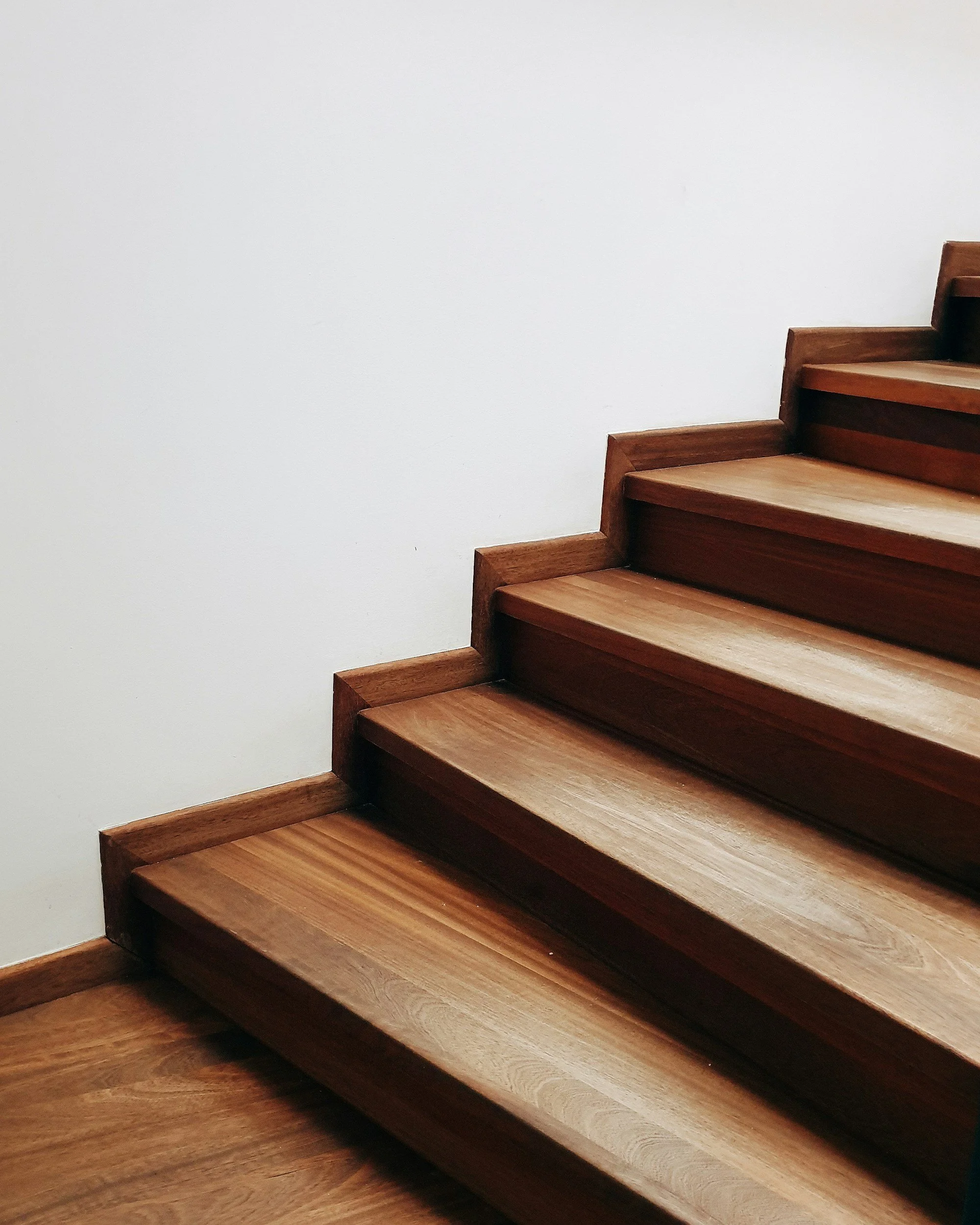 A wooden staircase with polished steps next to a plain white wall.