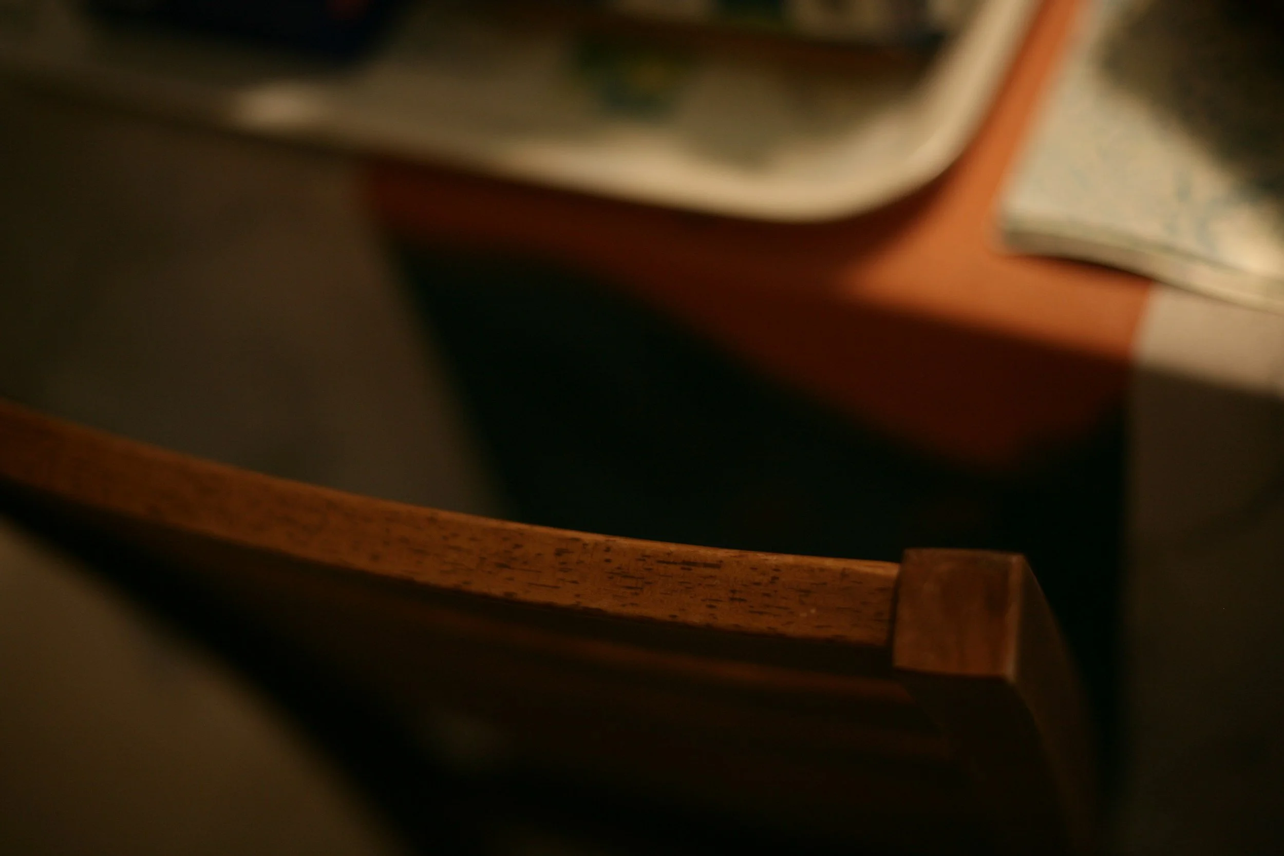 Blurred close-up of the corner of a wooden table with objects on its surface, including a book or magazine with patterned pages.