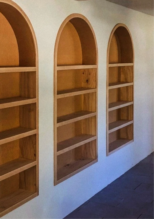 Three wooden arch-shaped shelves built into a white wall, each with five compartments.