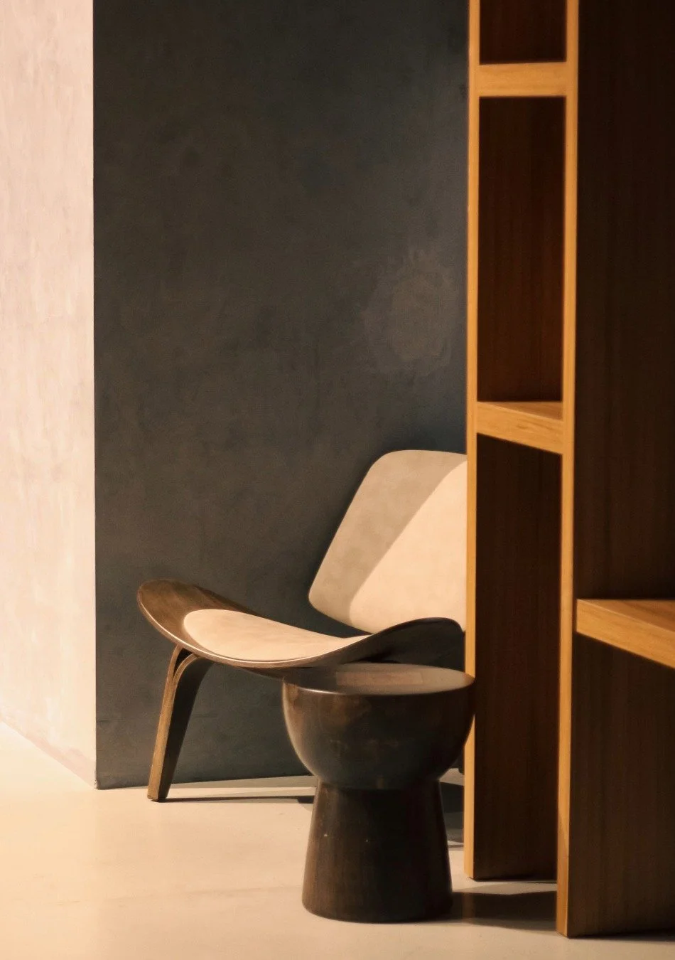 Modern interior with a black planter-style chair next to a wooden shelving unit against a dark wall.