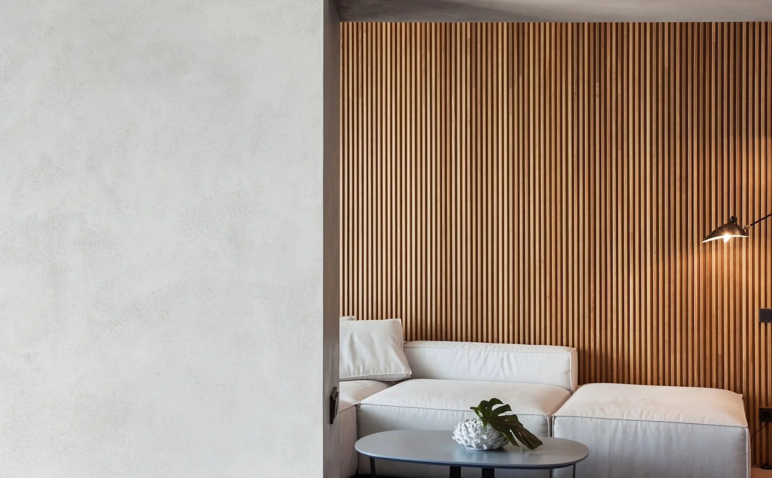 Modern living room with a white couch, a small coffee table with a decorative vase and leaf, a wooden accent wall, and a black floor lamp.