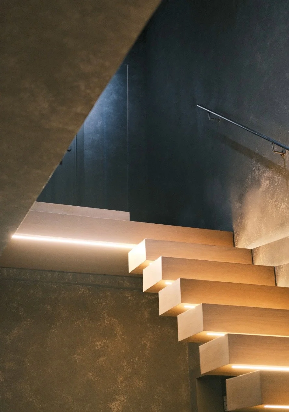Modern staircase with wooden steps and under-step lighting in a dimly lit interior space.