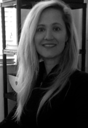 A smiling woman with long, wavy blonde hair looking at the camera, indoors with shelves in the background.