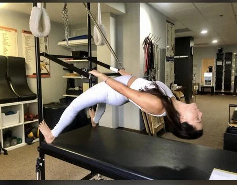 A woman performing a backbend stretch on a massage table in a physiotherapy or chiropractic clinic.