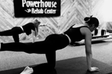 Person performing a plank exercise with a resistance band attached to a wall at Powerhouse Rehab Center.