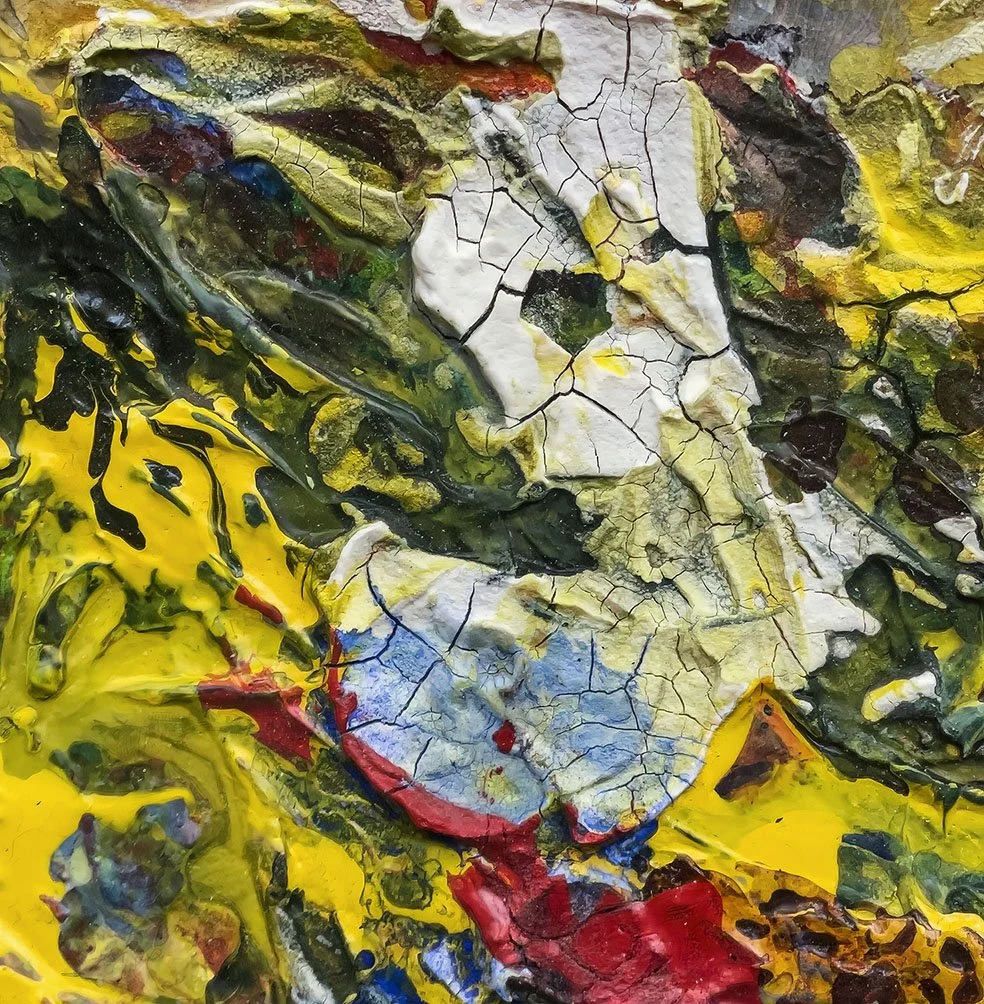 Close-up of a textured abstract painting with thick layers of yellow, black, white, red, blue, and green paint, showing cracks and crackles.