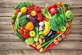 Fresh assorted vegetables and fruits arranged in a heart shape on a wooden surface