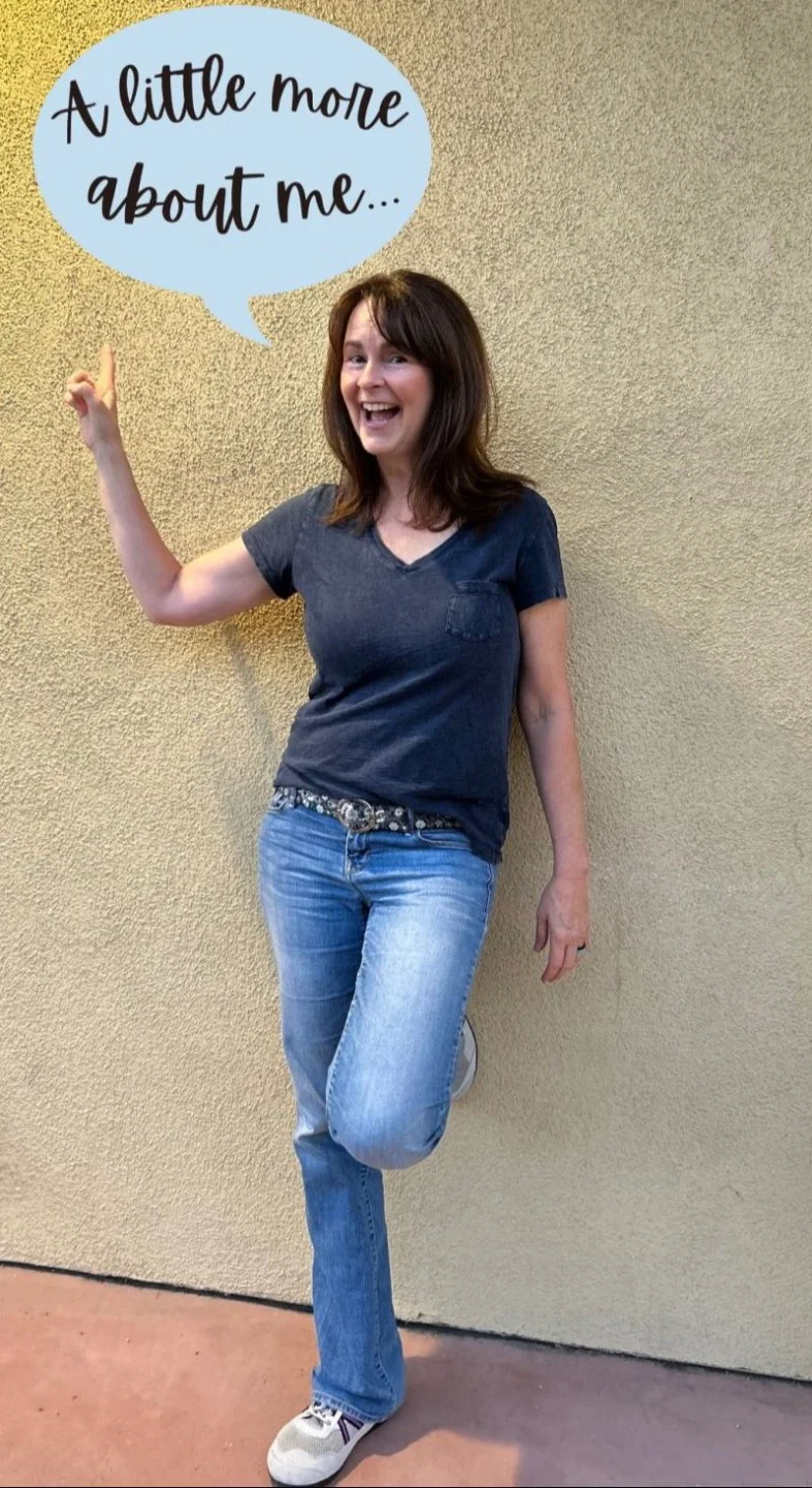 A woman standing against a textured beige wall, smiling and pointing up with her right hand. She is wearing a dark grey t-shirt, light blue jeans, and white sneakers. A speech bubble above her head contains the text, 'A little more about me...'.