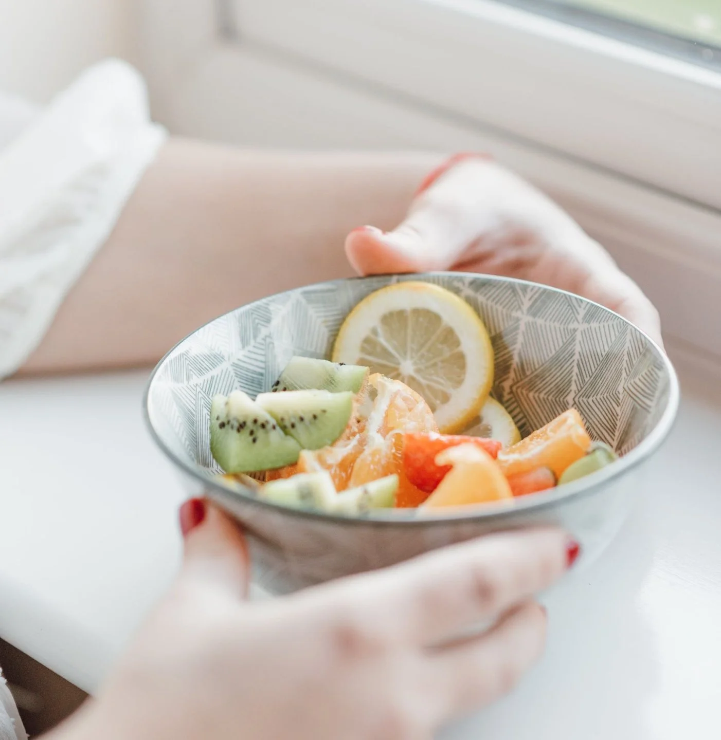 Person holding a bowl of mixed sliced fruits including lemon, kiwi, orange, and watermelon.