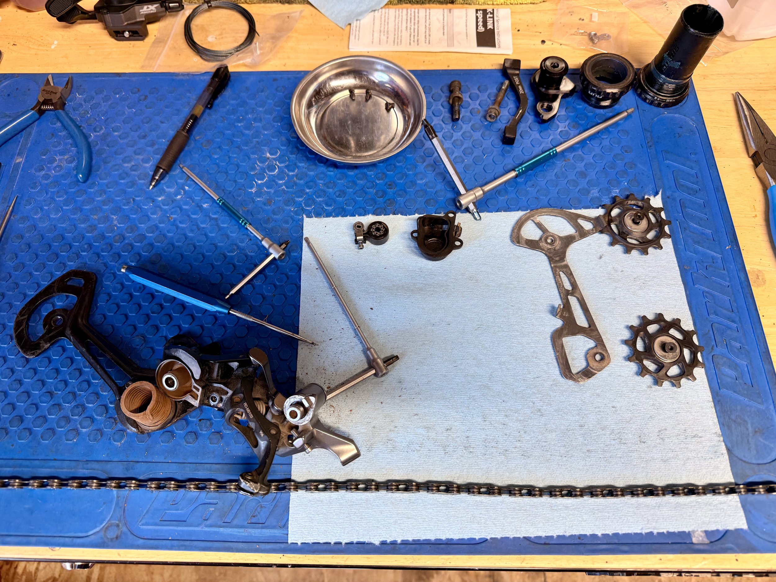 A workbench with bicycle parts and tools, including gears, chain, and wrenches, on a blue mat.